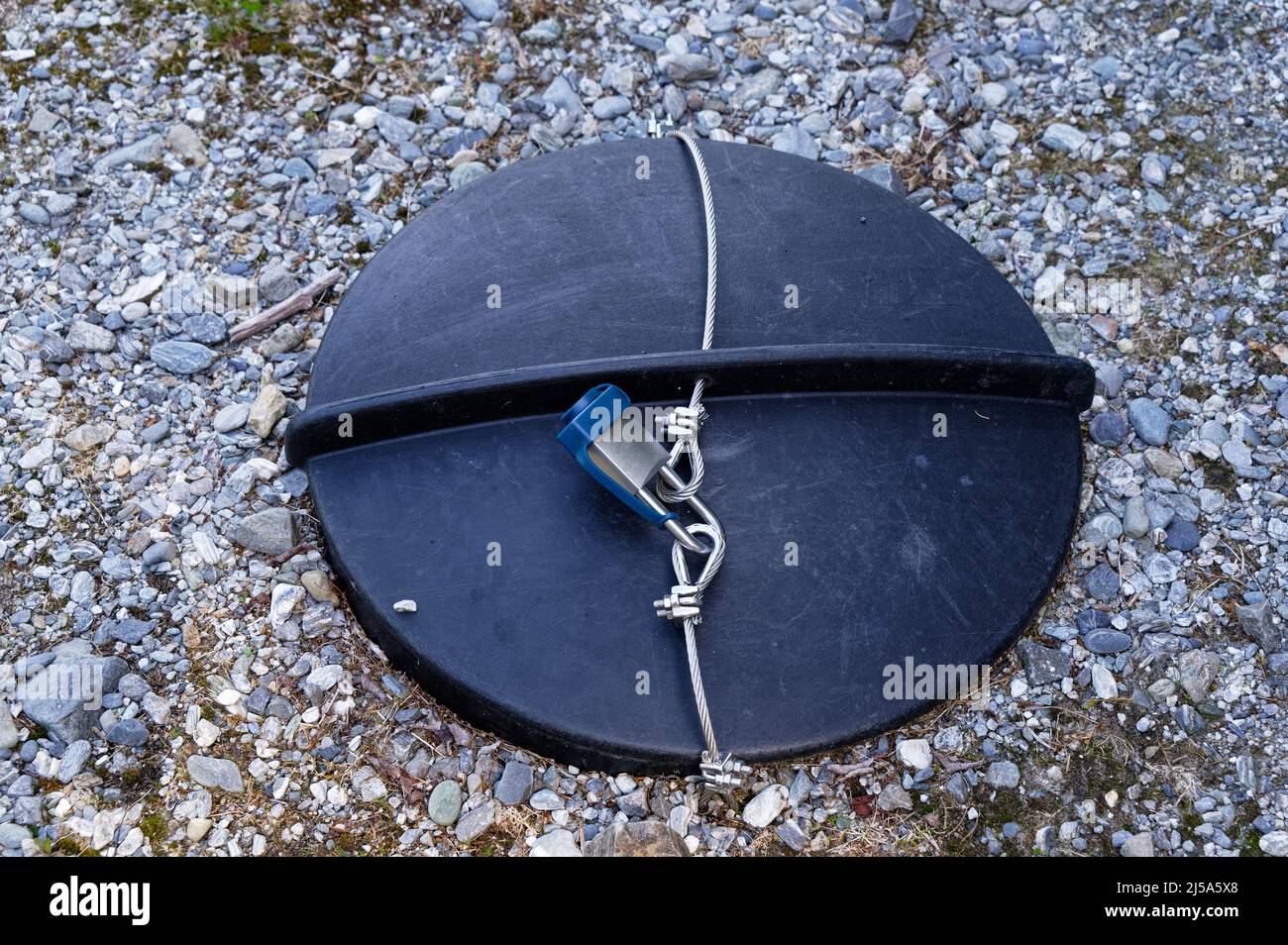 Ein Schloss und ein Stahlkabel sichern den Deckel eines unterirdischen Tanks Stockfoto