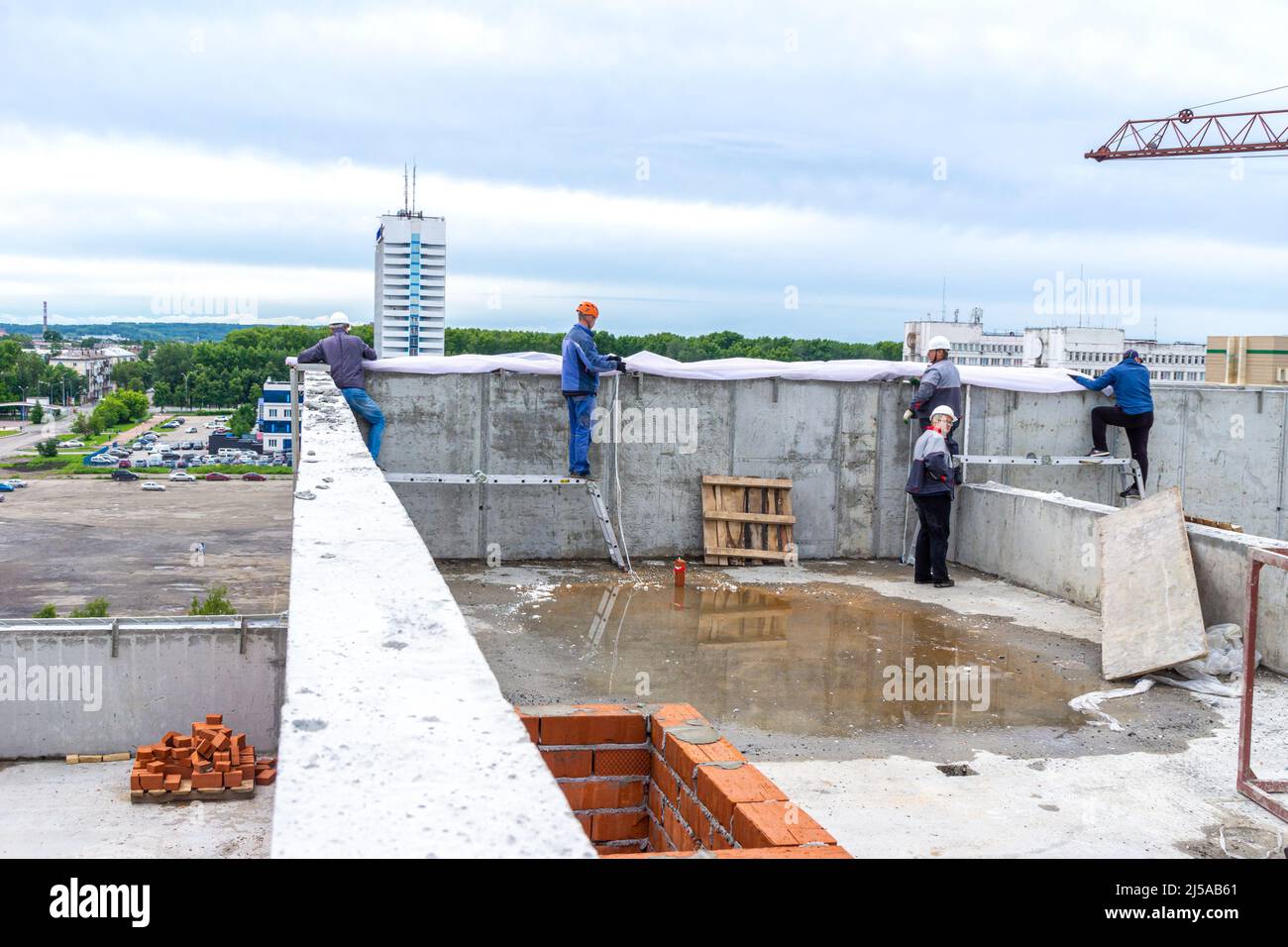 Kemerowo, Russland - 24. juni 2021. Auf dem Dach der Bauarbeiter ziehen schützende Konstruktionsgewebe der falschen Fassade, die Bauherren vor schützen wird Stockfoto