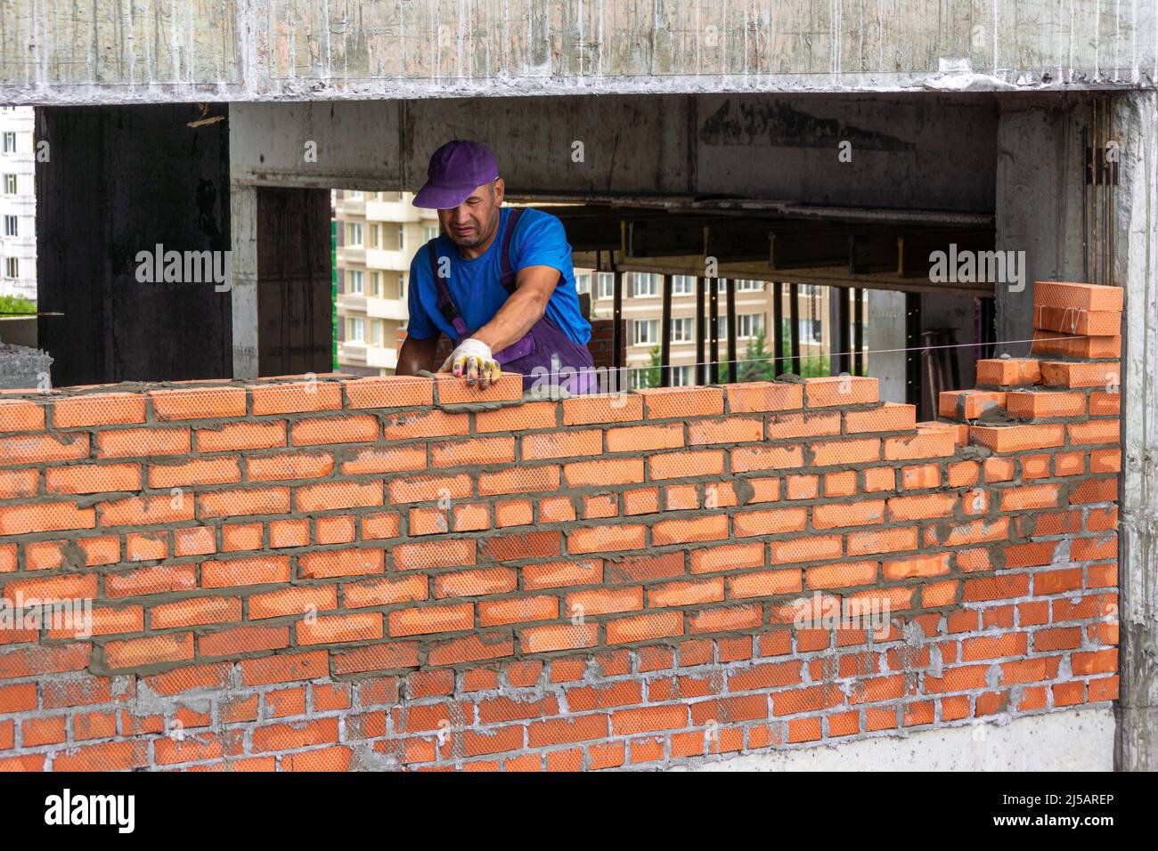 Kemerowo, Russland - 24. juni 2021. Maurer Arbeiter Mauerwerk Ziegel auf Mörtel, Gebäude Trennwand in Gebäude mit Beton Hauptrahmen, selektive FOC Stockfoto