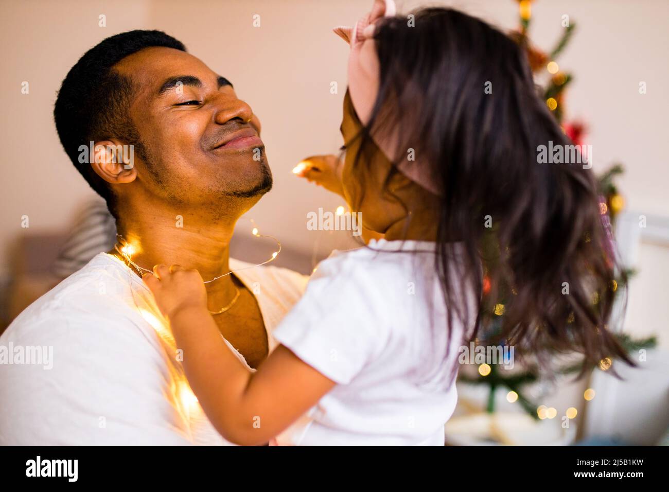 Glücklicher gemischter Vater und schönes Kind im fröhlichen Weihnachtsmorgen im Schlafzimmer Stockfoto