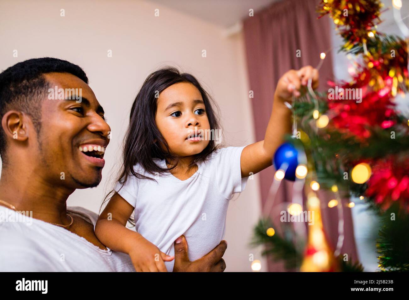 Glücklicher gemischter Vater und schönes Kind im fröhlichen Weihnachtsmorgen im Schlafzimmer Stockfoto