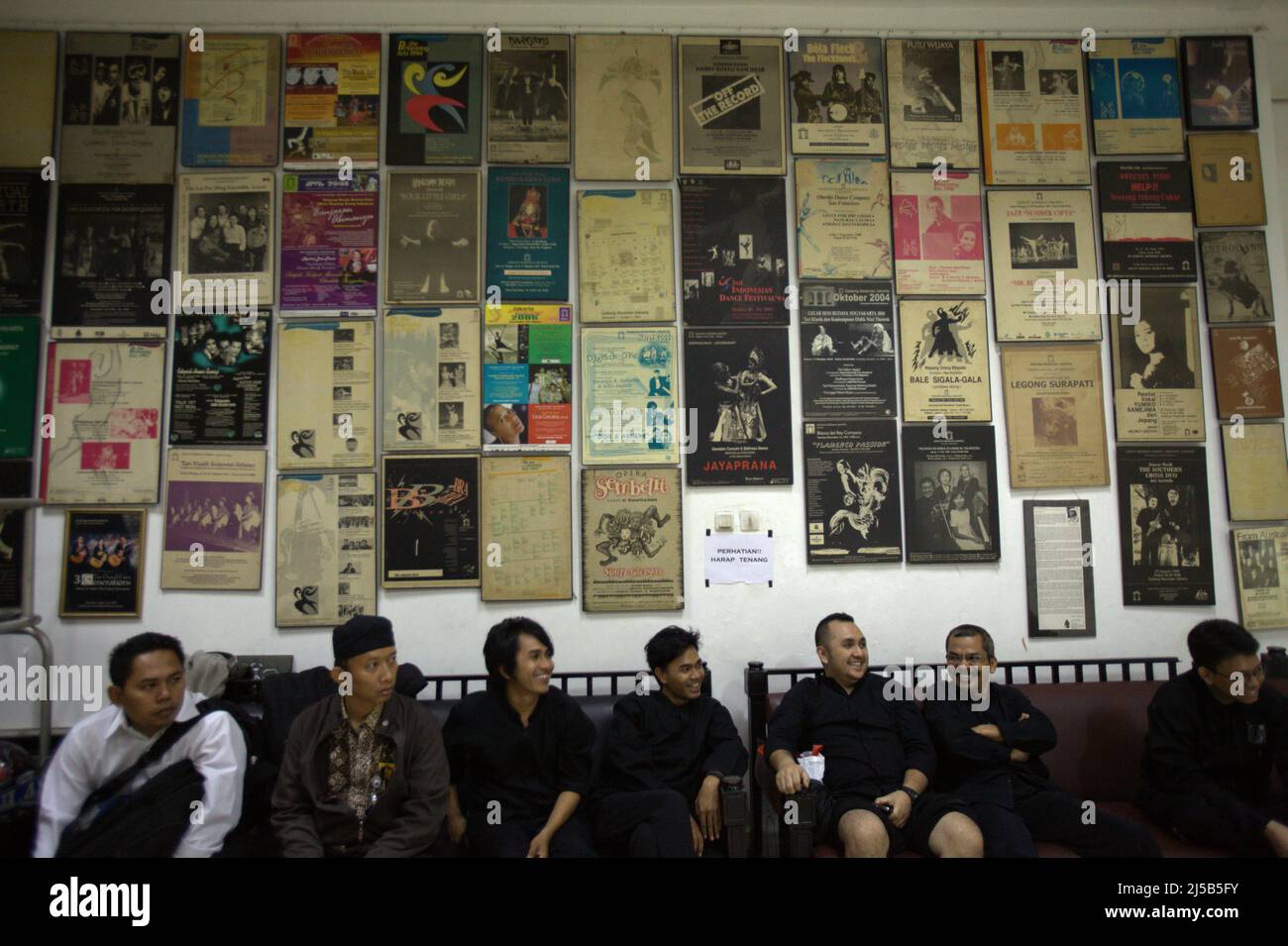 Menschen sitzen vor einer Wand, die mit Werbeplakaten von Kunstaufführungen geschmückt ist, die am 15. Juni 2011 in Jakarta, Indonesien, auf der Bühne der Galleri Kesenian Jakarta (Jakarta Art Gallery) erschienen waren. Stockfoto