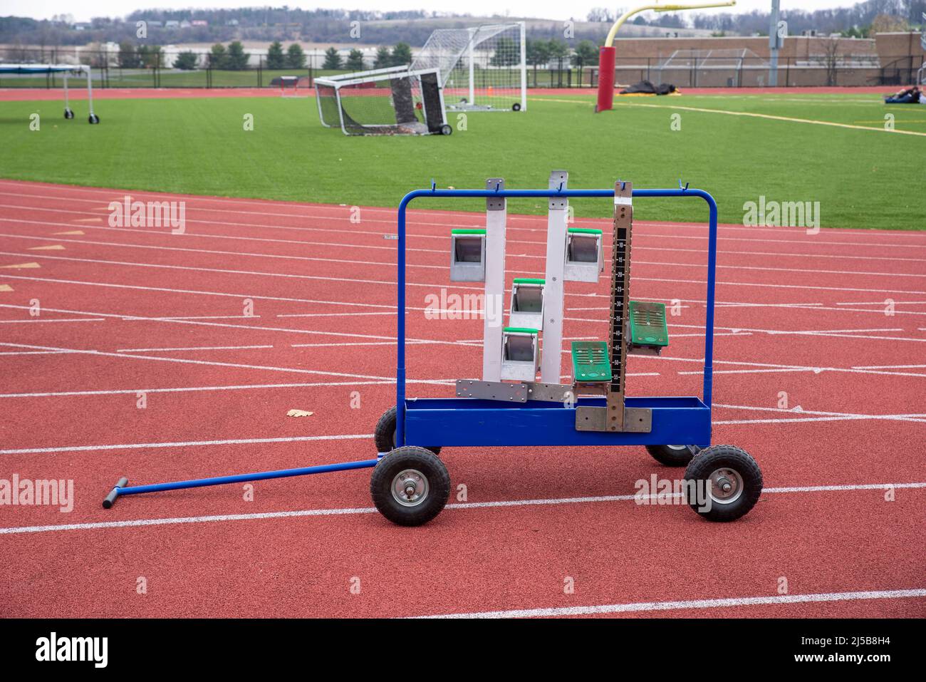 Ein Rolling Metal Sportgeräte Rack mit Track and Field Running Rennen Startblöcke auf einer leeren athletischen Strecke mit Spurmarkierungen. Im Freien aufgenommen i Stockfoto