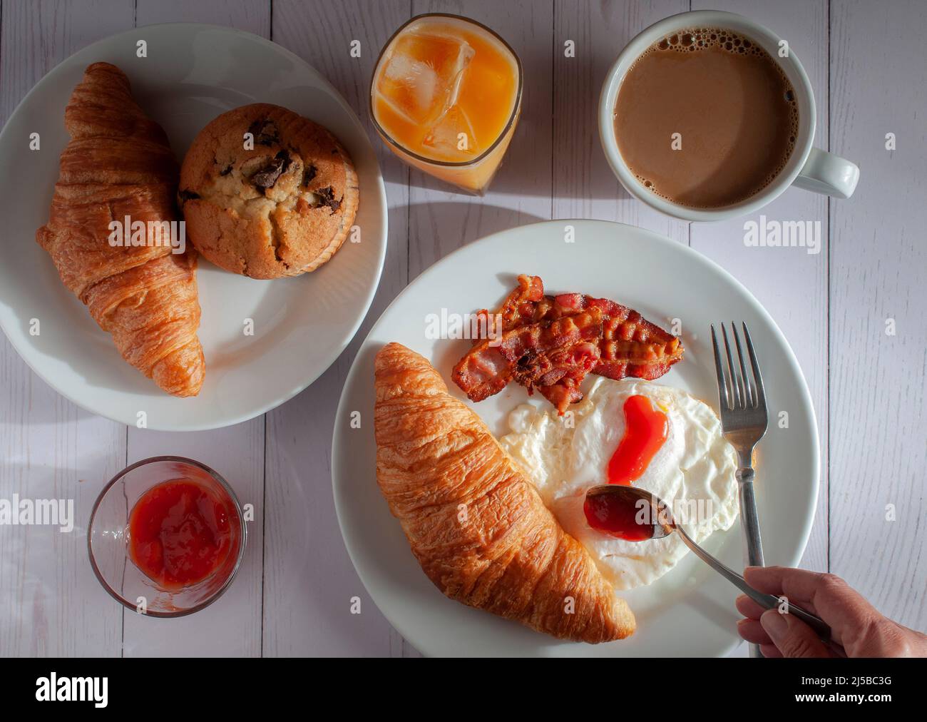 Amerikanisches Frühstück mit übermäßigen Eiern, Speck, Brot, Orangensaft und Rahmkaffee auf einem weißen Tisch mit der Morgensonne, die aus dem Fenster kommt Stockfoto