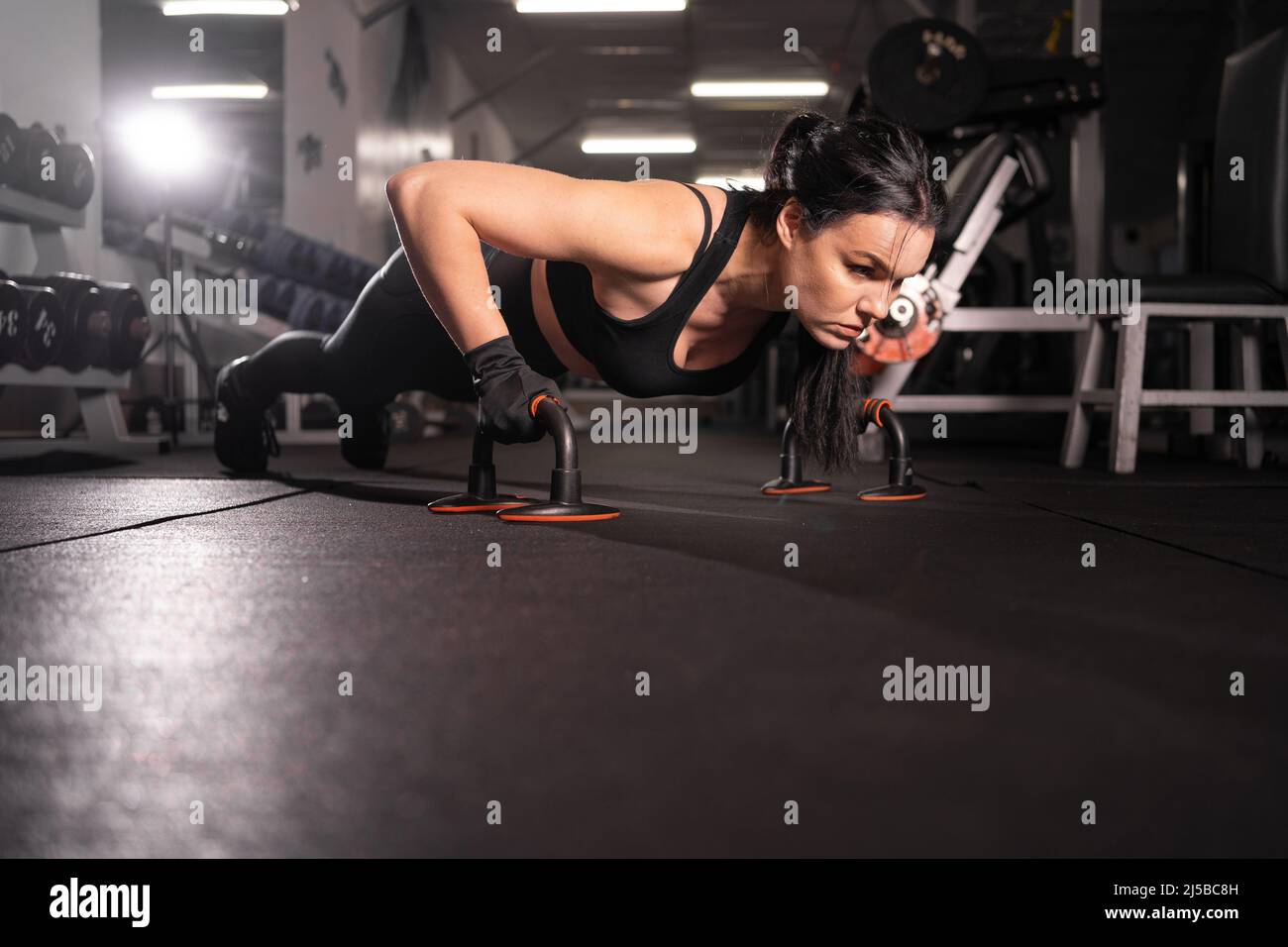 Seitenansicht eines schönen athletischen Mädchens, das in einem schwarzen Sporttop und Strumpfhosen gekleidet ist und während eines harten Trainings im Fitnessstudio mit Liegestützen trainiert. Gesunde Lif Stockfoto