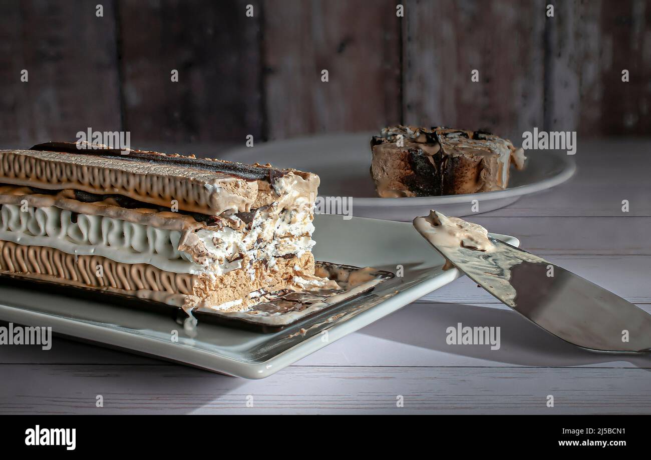 Ein rechteckiger Kaffee-Moka-Eiskuchen auf einem weißen Teller mit einer Scheibe im Hintergrund Stockfoto