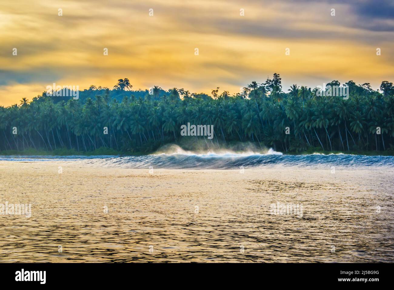 Palmengesäumter Strand auf einer tropischen Insel in der Morgendämmerung oder Abenddämmerung, vom umgebenden Ozean aus gesehen Stockfoto