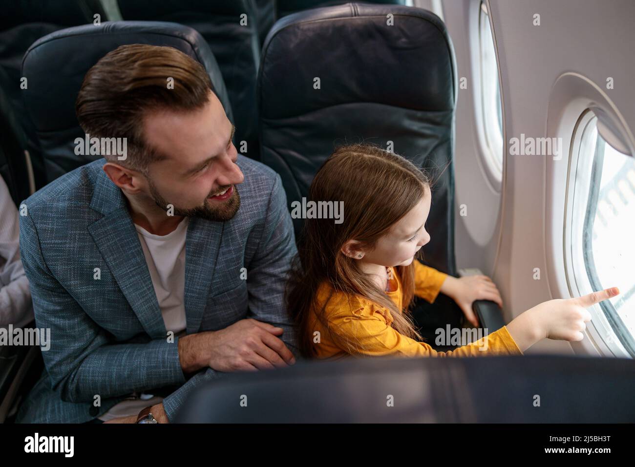 Fröhlicher Mann und seine Tochter blicken aus dem Fenster im Flugzeug Stockfoto