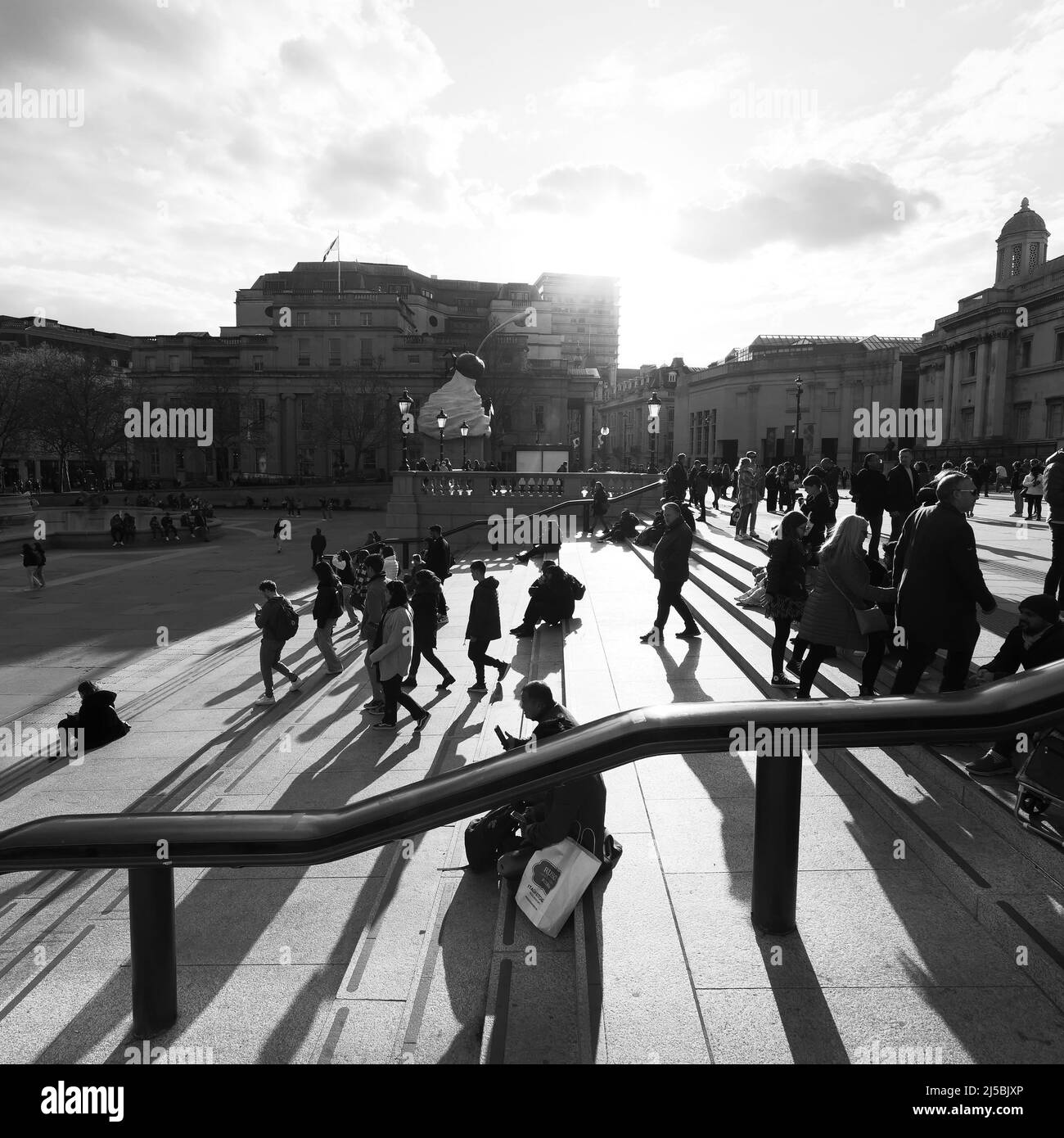 Touristen, die auf dem Trafalgar Square mit dem vierten Sockel hinter der Treppe sitzen und spazieren. Monochrom. London. Stockfoto
