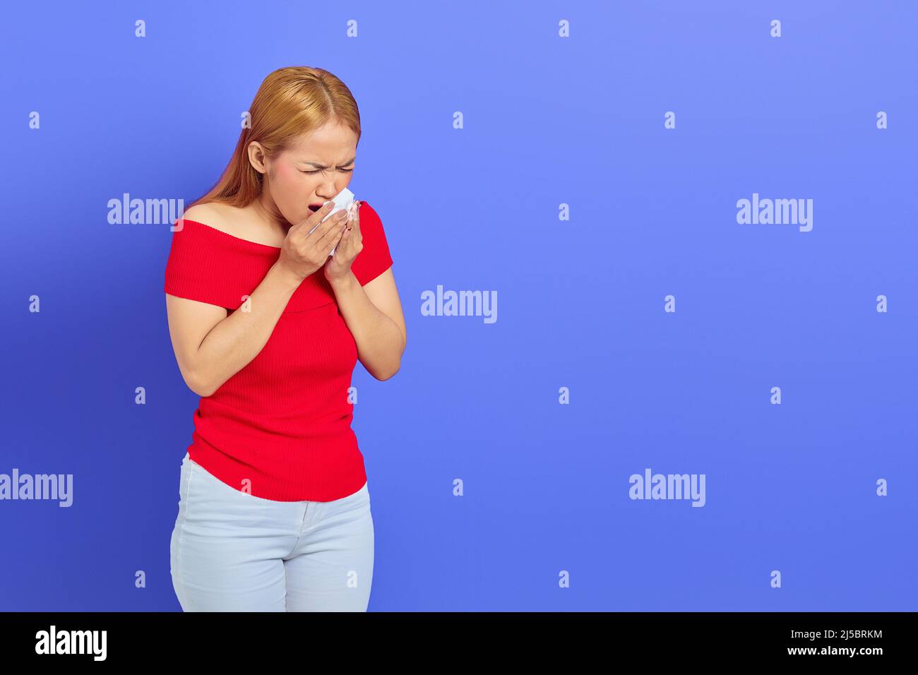 Porträt der schönen jungen asiatischen Frau niesen, sie verwendet Gesichtsgewebe Papier über ihre Nase und Mund isoliert auf lila Hintergrund. Stockfoto