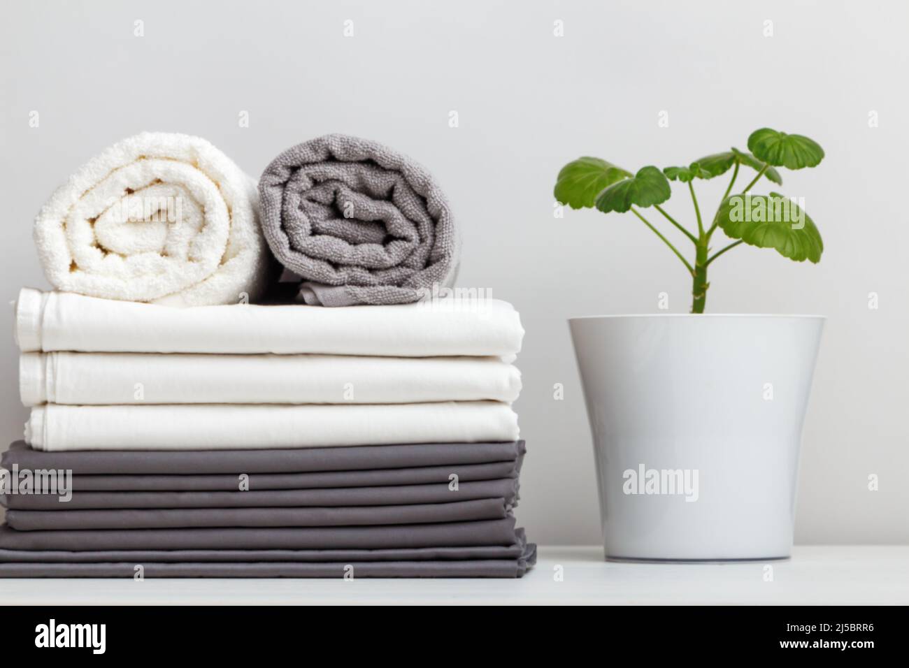 Ein Stapel grauer und weißer Bettwäsche, Bettwäsche und Handtücher auf dem Tisch. Pflanze in den Topf Stockfoto