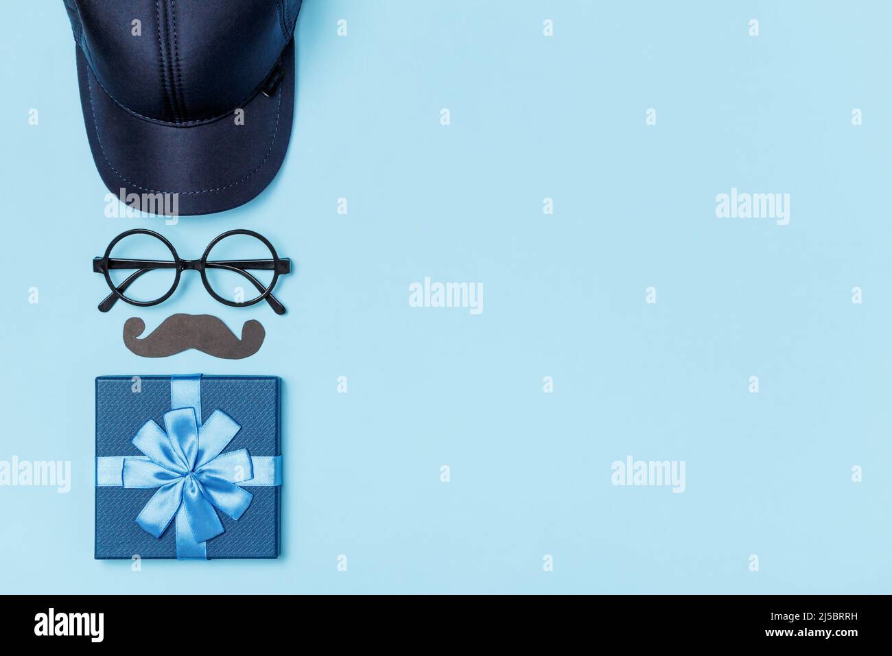 Vatertag Konzept. Geschenk Krawatte Brille Schnurrbart Baseballmütze auf blauem Hintergrund mit Kopieplatz Stockfoto