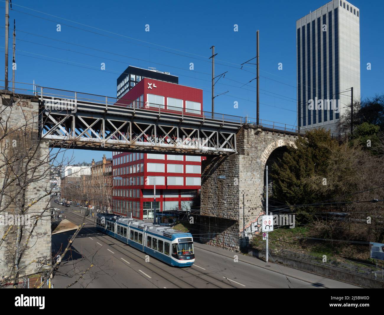 Zürich, Schweiz - März 5. 2022: Eine Trambahn, die unter einer Eisenbahnbrücke in einem Geschäftsviertel fährt Stockfoto