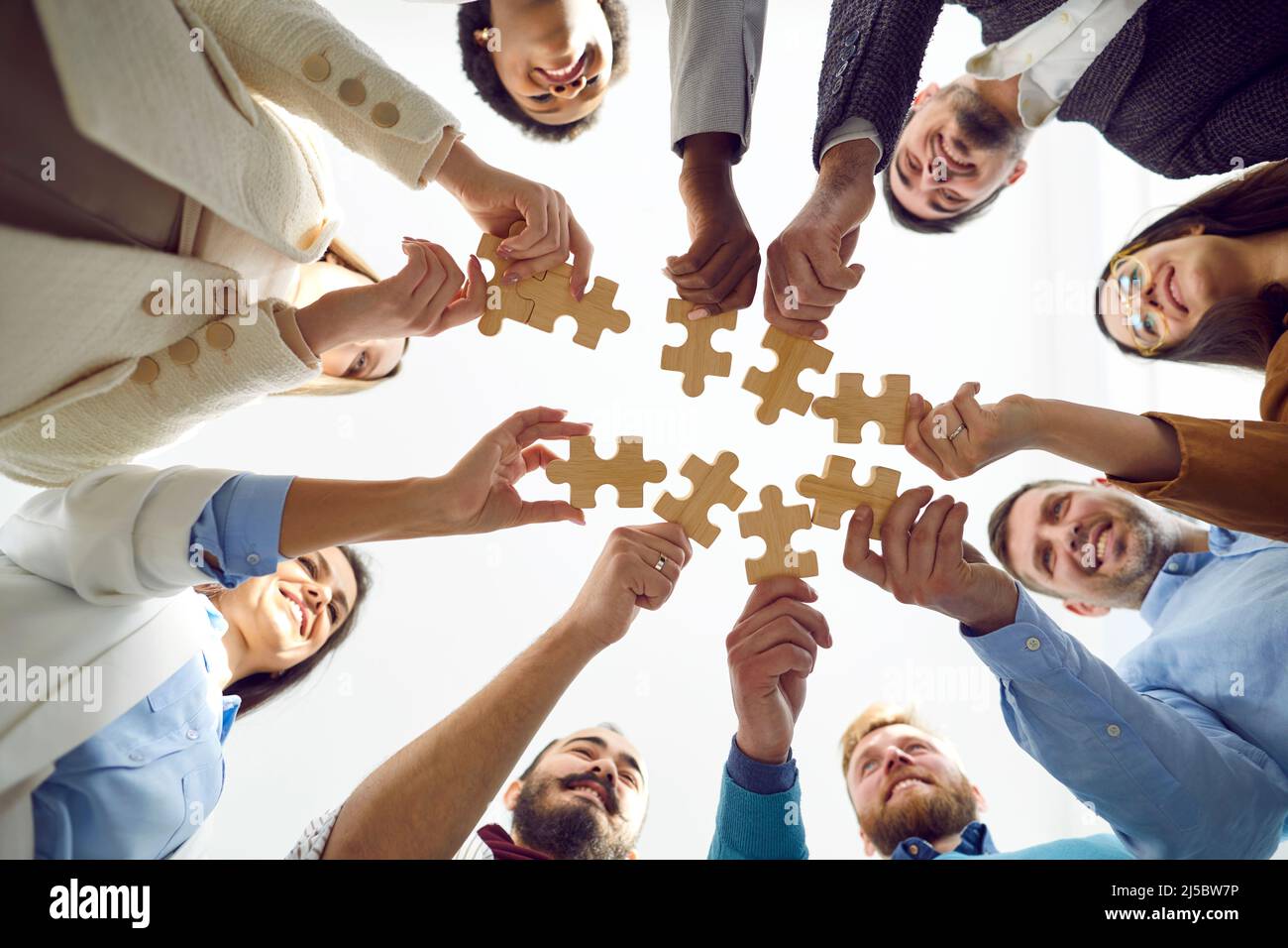Glückliche verschiedene Menschen stellen Holzpuzzles zusammen, die Teamwork symbolisieren. Stockfoto