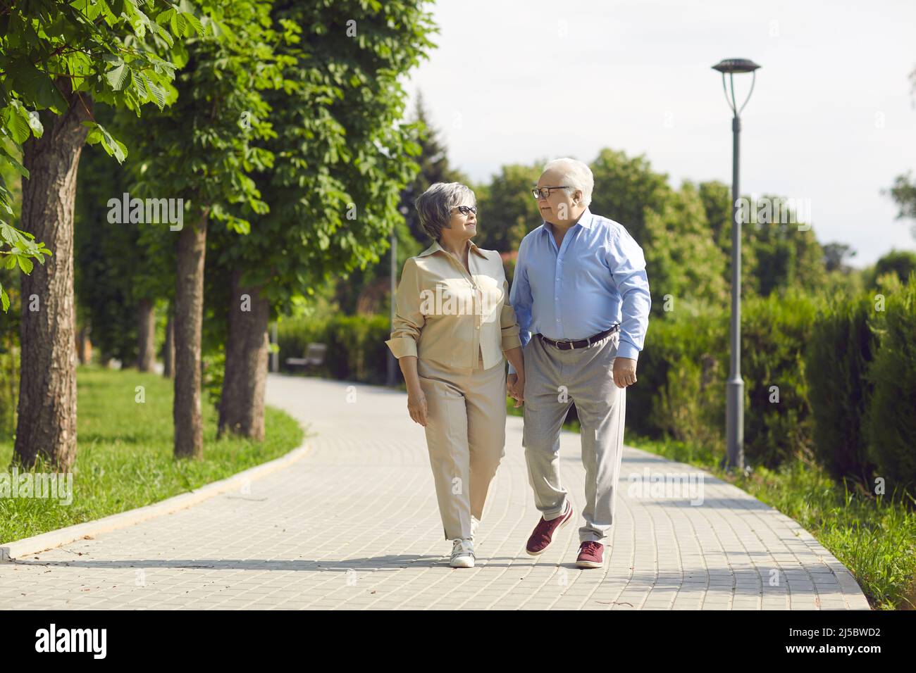 Fröhliches Seniorenpaar, das sich in einem Stadtpark gut amüsiert, zu Fuß geht, lacht und einen sonnigen Tag genießt. Stockfoto