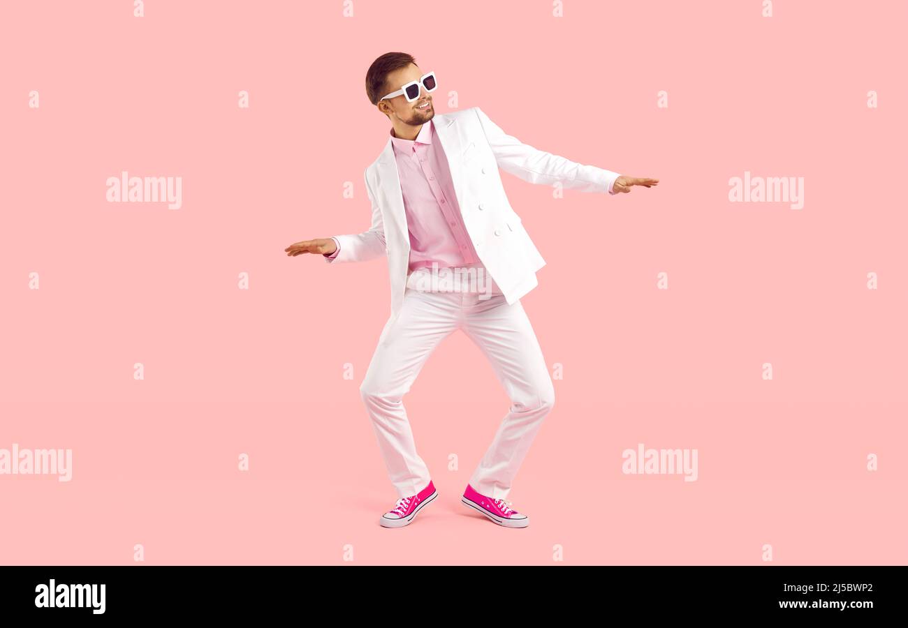 Fröhlicher, cooler junger Mann im Anzug zeigt lustige Tanzbewegungen isoliert auf rosa Hintergrund. Stockfoto