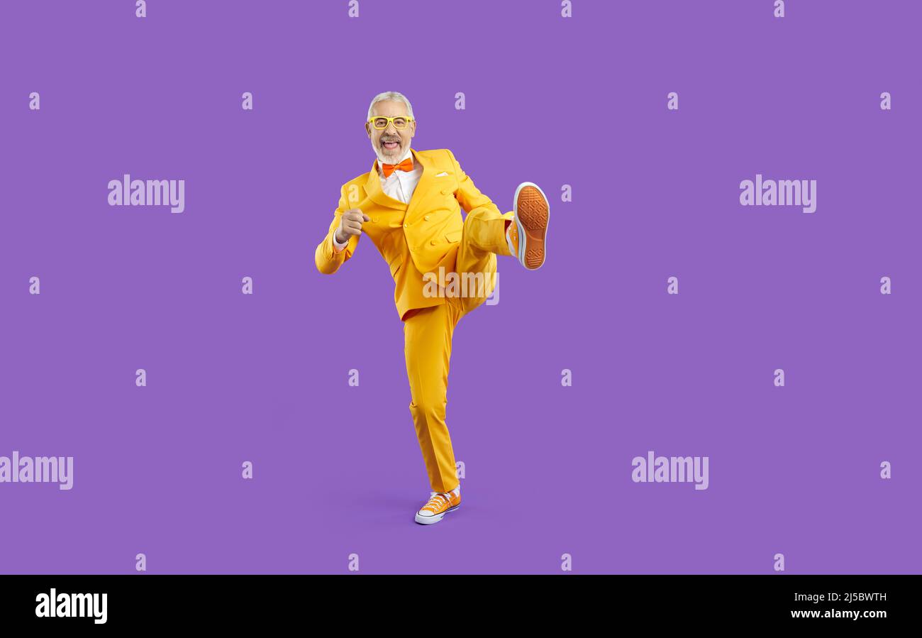 Fröhlicher exzentrischer und lustiger älterer Mann in gelbem Anzug isoliert auf violettem Hintergrund. Stockfoto