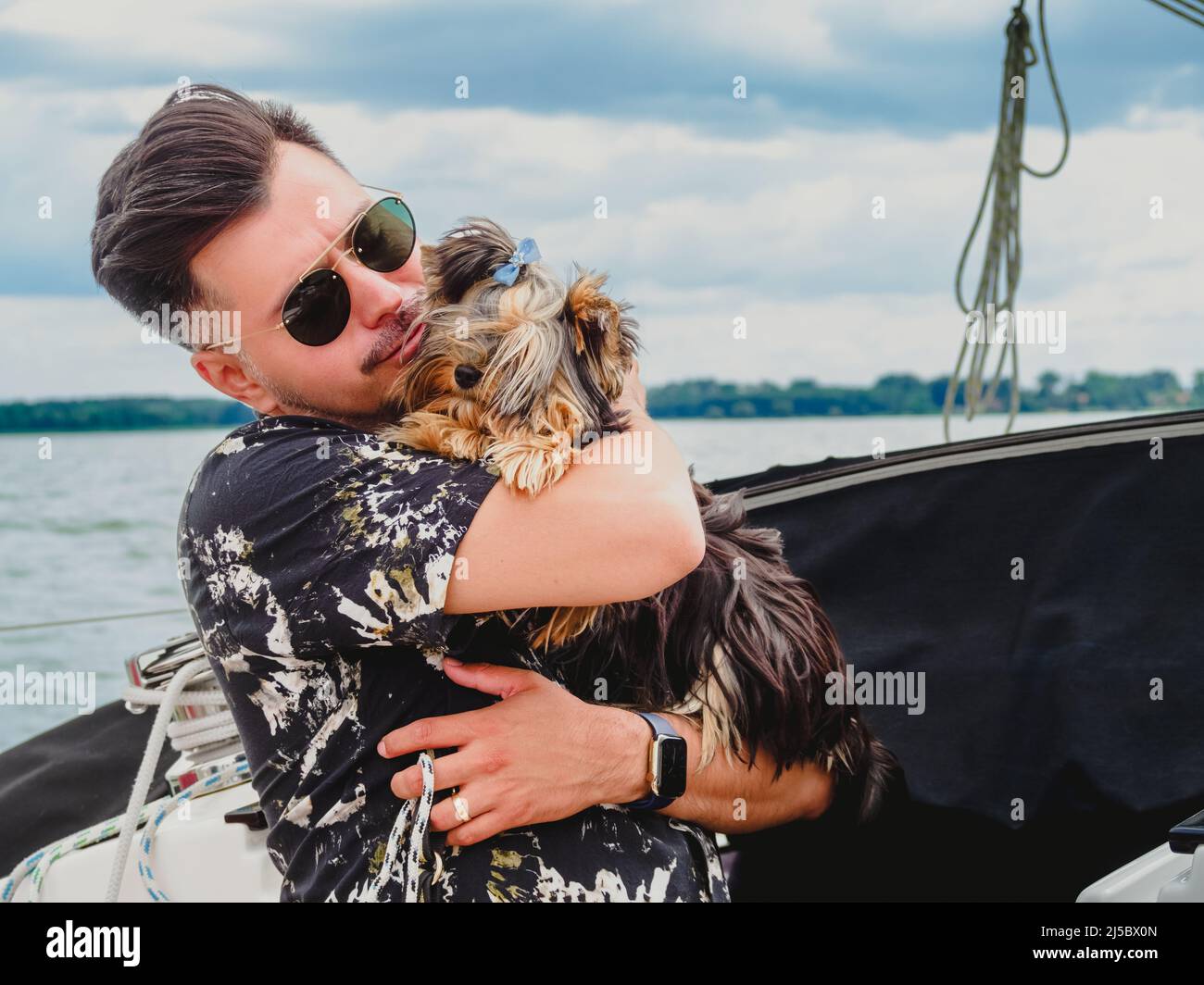 Ein hübscher Mann umarmt und küsst seinen kleinen Hund yorkshire Terrier Stockfoto