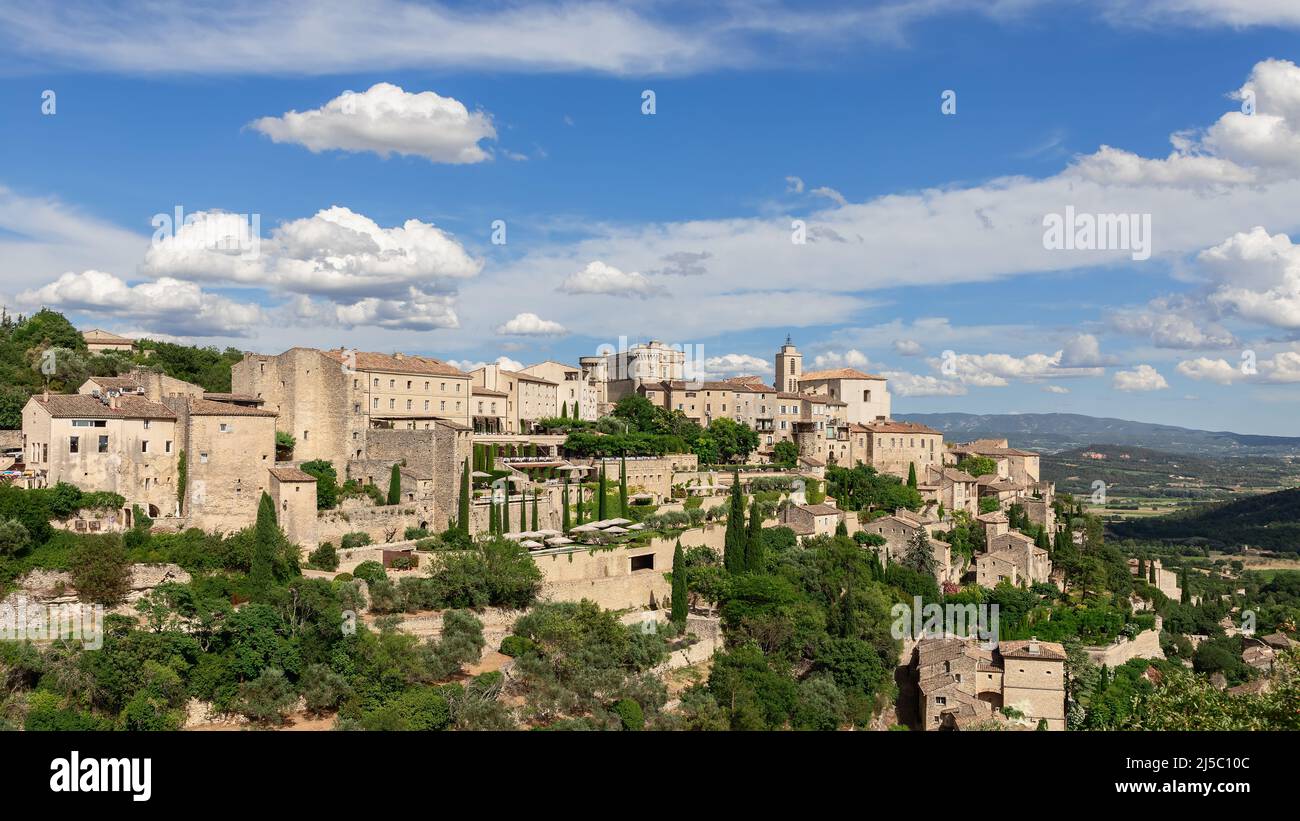 Atemberaubend malerischer Himmel mit schwebenden weißen Wolken über dem mittelalterlichen Dorf Gordes, Felsen und dem Luberon-Tal. Vaucluse, Provence, Frankreich Stockfoto
