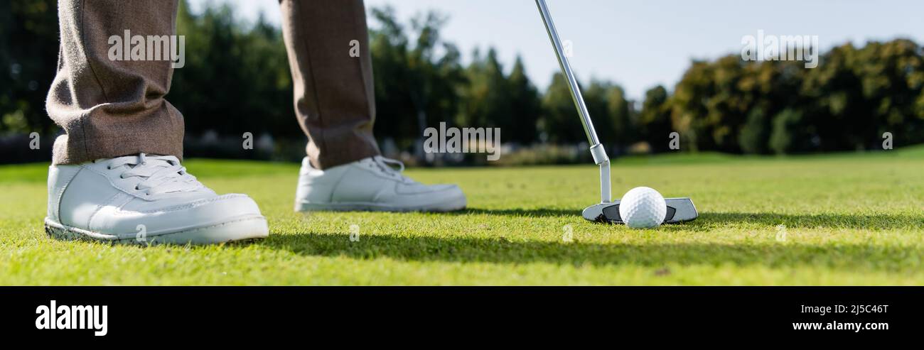 Beschnittene Ansicht des Mannes in weißen Sneakers, der Golf auf dem Rasen spielt, Banner Stockfoto