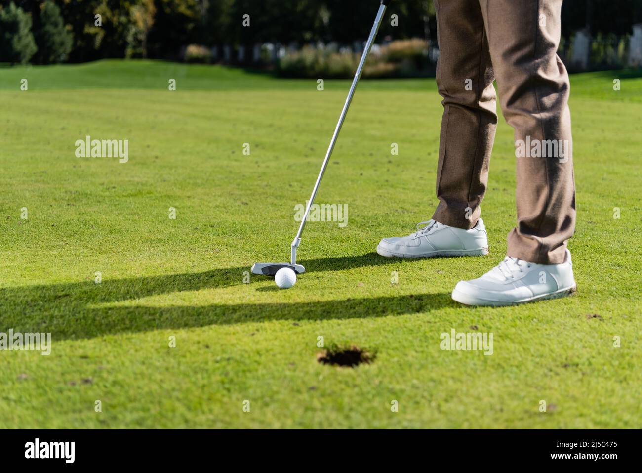 Beschnittene Ansicht eines Mannes in weißen Sneakers, der auf dem Rasen Golf spielt Stockfoto