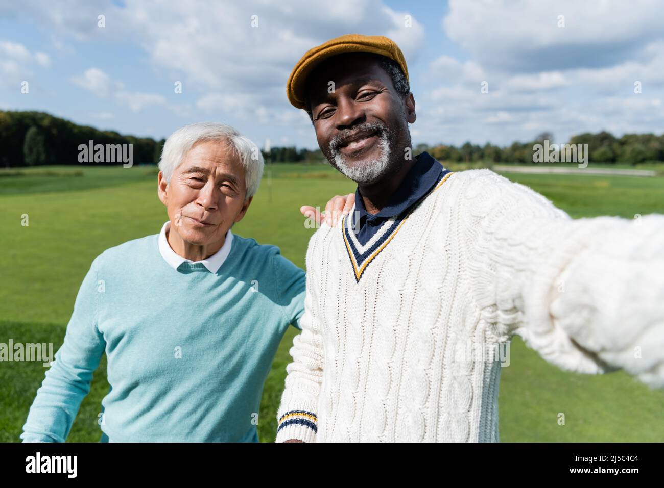 Ein zufriedener afroamerikanischer Mann, der Selfie mit einem älteren asiatischen Freund des Golfplatzes gemacht hat Stockfoto