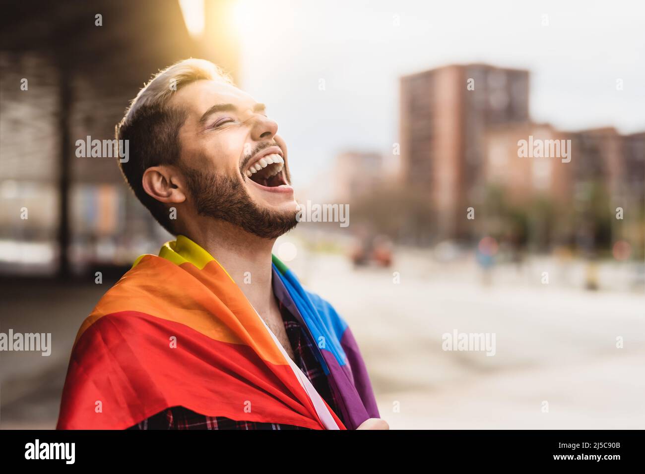 Glücklicher schwuler Mann, der Spaß hat, das Symbol der LGBTQ-Gemeinschaft mit der Regenbogenflagge zu halten Stockfoto