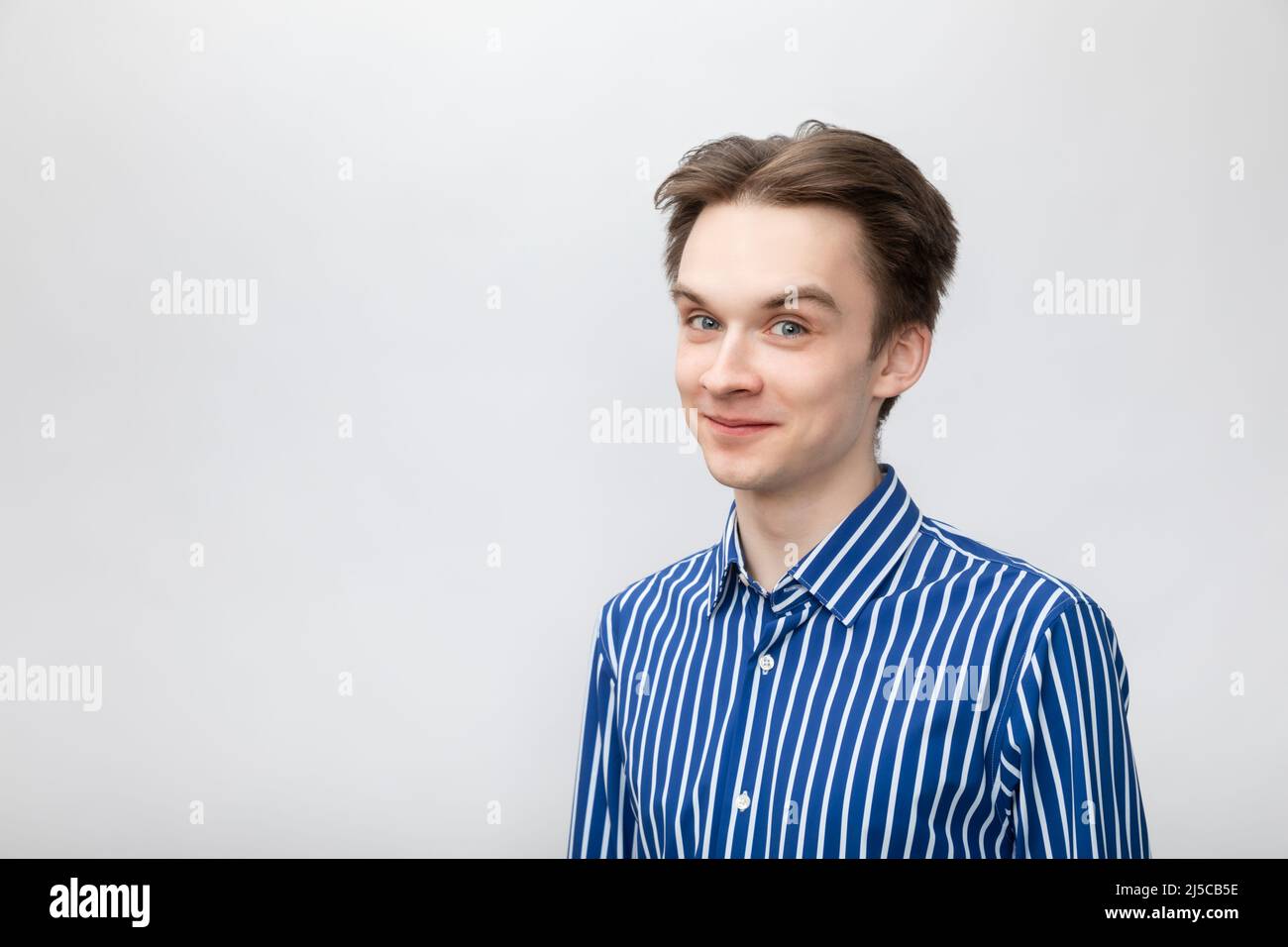 Porträt eines fröhlichen Teenagers mit blau-weißem gestreiftem Knopfhemd und Blick auf die Kamera. Studio auf grauem Hintergrund aufgenommen Stockfoto