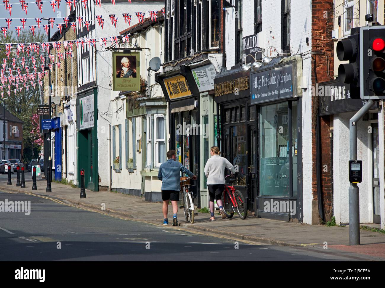 Mann und Frau schieben Fahrräder entlang der High Street in Cottingham, East Yorkshire, England Stockfoto