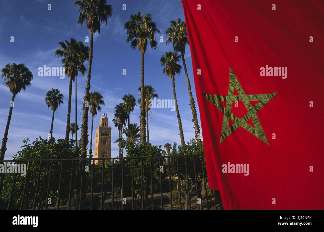 09.11.2010, Marrakesch, Marokko, Afrika - Eine rote marokkanische Nationalflagge mit Stern verdunkelt den Blick durch den Lalla Hasna Park mit seinen Palmen und dem Minarett der Koutoubia Moschee im Hintergrund. [Automatisierte Übersetzung] Stockfoto