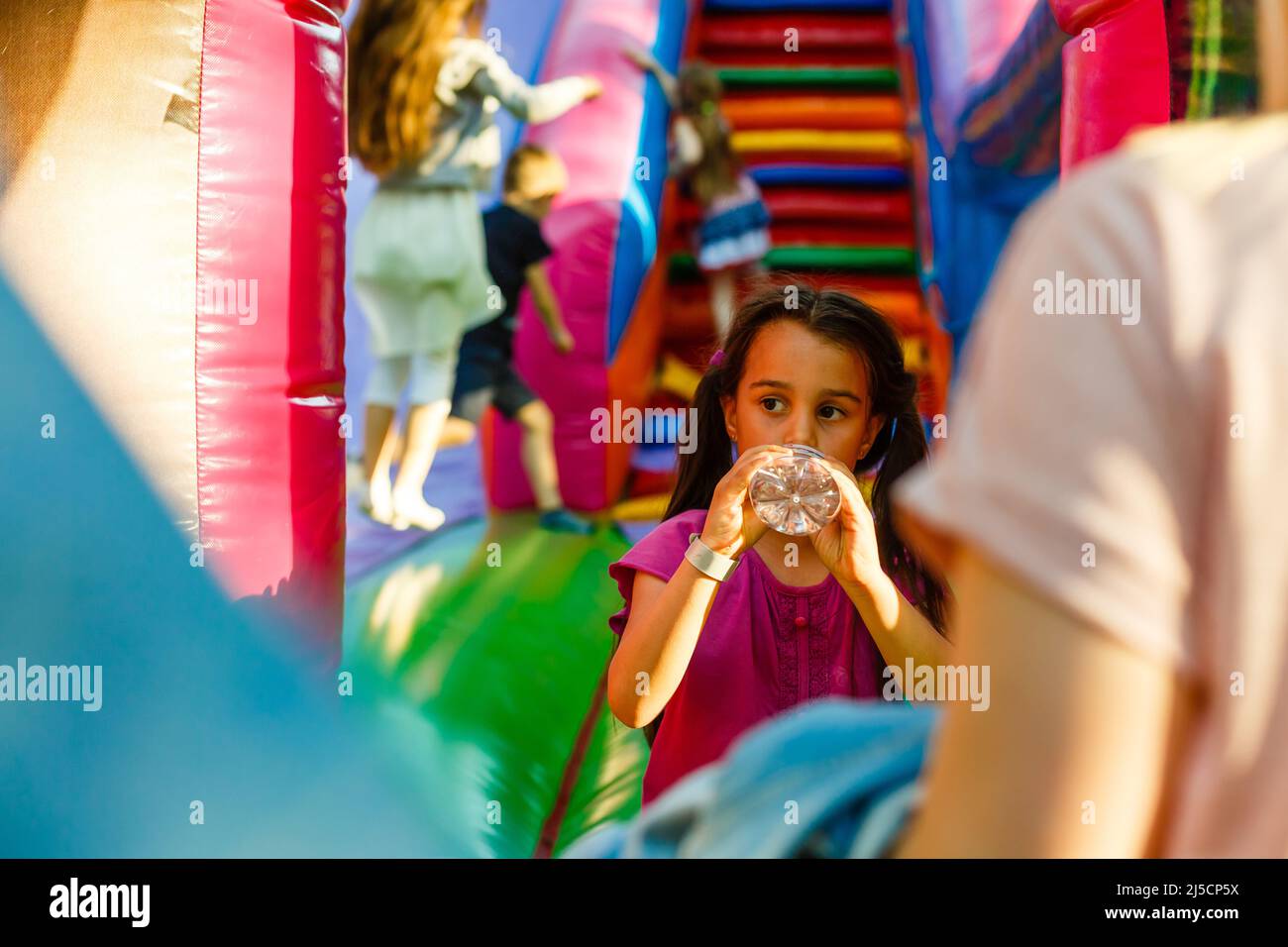 Kleines Mädchen trinkt Wasser auf einem aufblasbaren Trampolin Stockfoto