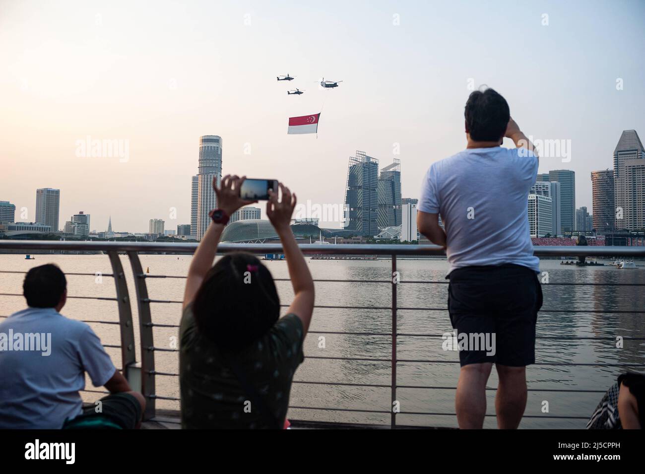 07/21/2018, Singapur, Republik Singapur, Asien - Zuschauer beobachten, wie Hubschrauber der Luftwaffe (RSAF) während eines Trainingsfluges eine riesige Staatsflagge über Wolkenkratzer in Marina Bay fliegen, um sich auf den bevorstehenden Nationalfeiertag am 9. August vorzubereiten. [Automatisierte Übersetzung] Stockfoto