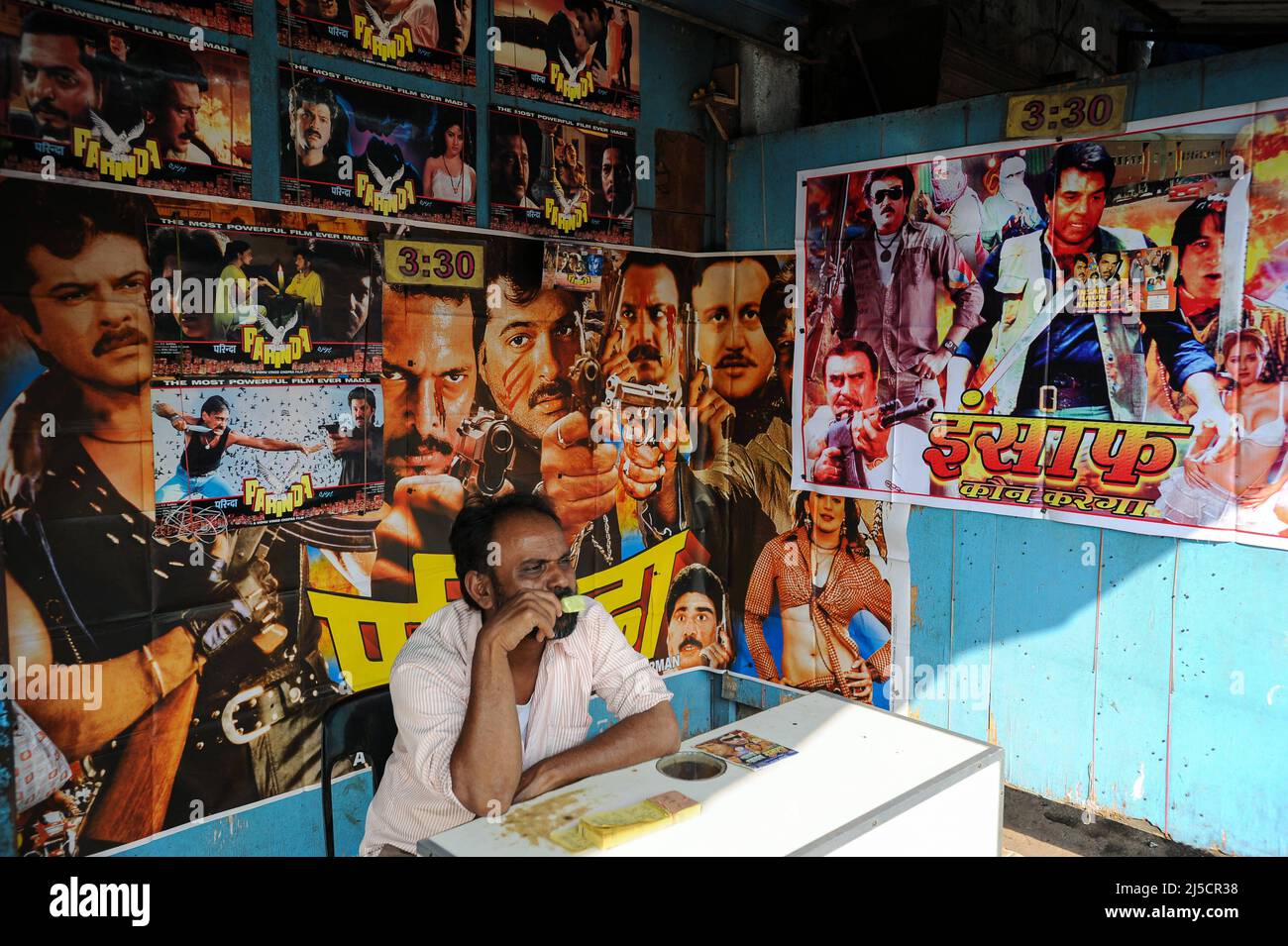 13.12.2011, Mumbai, Maharashtra, Indien, Asien - Ein Mann sitzt an der Kasse in einem kleinen Kino mit bunten Filmplakaten im Dharavi-Slum und isst ein Eis. Dharavi ist das größte Slum in der indischen Metropole. [Automatisierte Übersetzung] Stockfoto