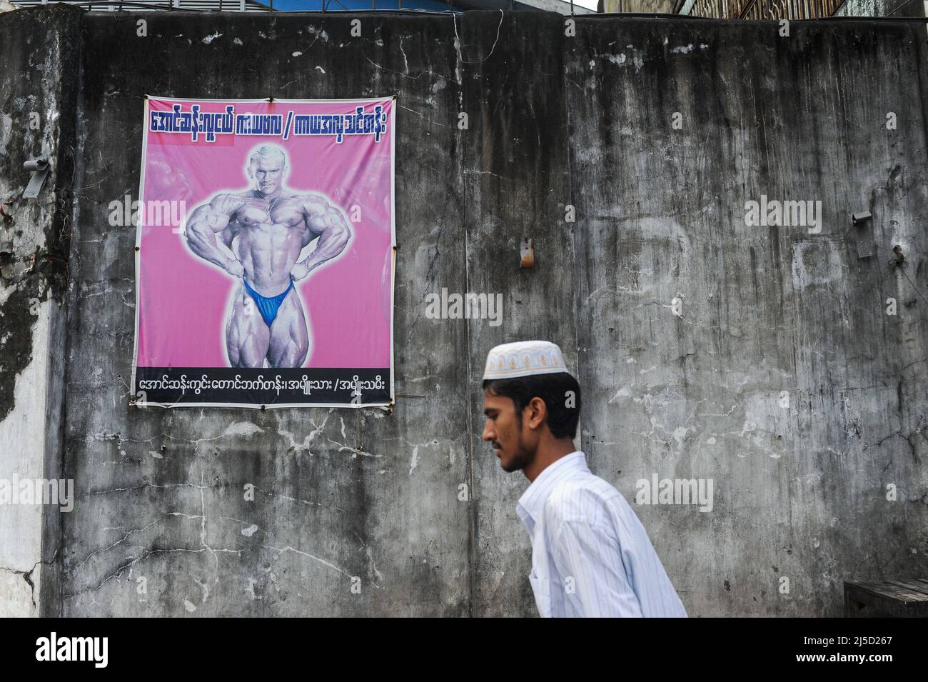 11.10.2013, Yangon, Myanmar, Asien - Ein muslimischer Mann in einem traditionellen takke-stil geht an einer Wand vorbei und zeigt ein Plakat, auf dem ein Bodybuilding-Ereignis angezeigt wird. [Automatisierte Übersetzung] Stockfoto