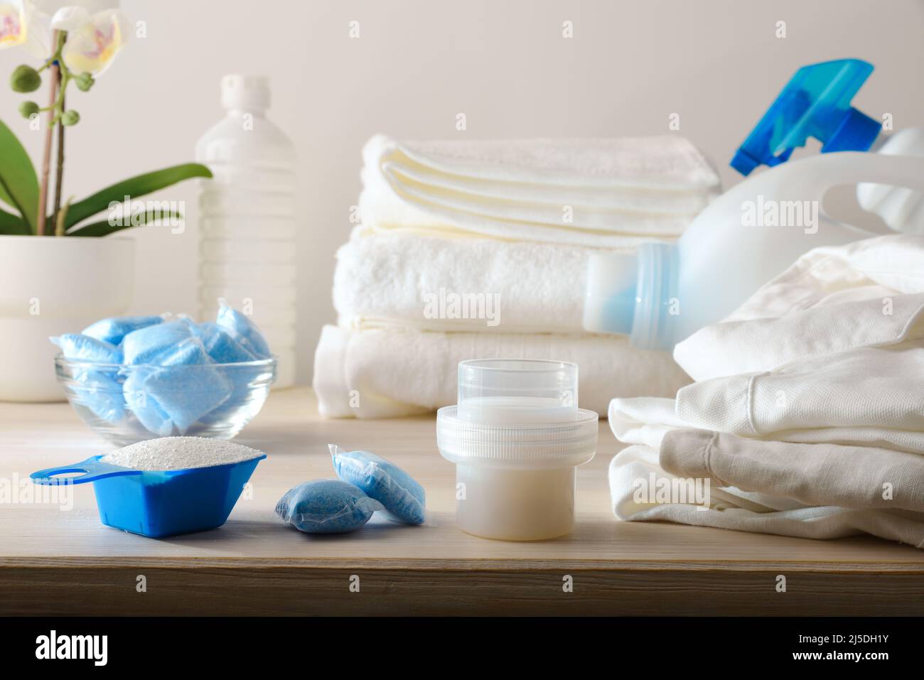 Detail von verschiedenen Arten von chemischen Produkten zum Waschen von Kleidung auf Holztisch und weiße Kleidung herum. Vorderansicht. Horizontale Zusammensetzung. Stockfoto