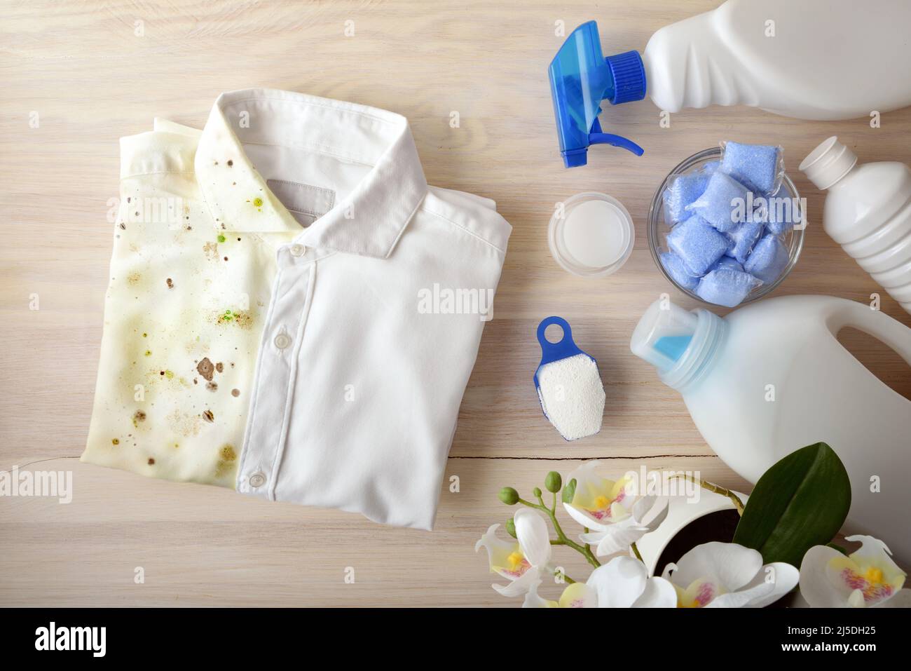 Vergleichendes Konzept des Waschens von Kleidung mit chemischen Produkten mit Hemd halb schmutzig halb sauber auf Holzbank mit verschiedenen Waschprodukten herum. T Stockfoto