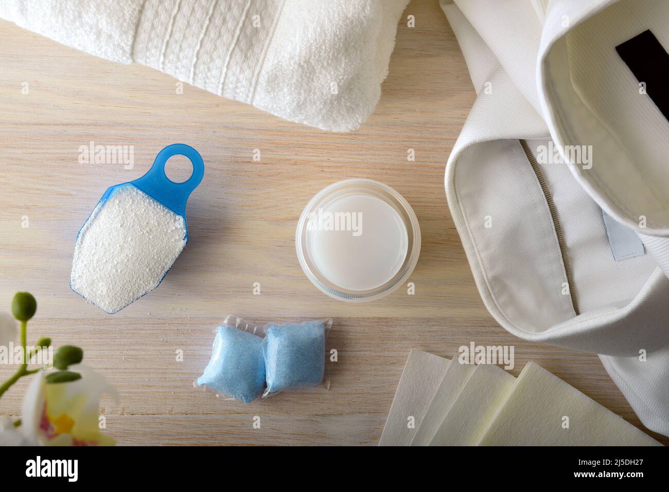 Detail von verschiedenen Arten von chemischen Produkten zum Waschen von Kleidung auf Holztisch und weiße Kleidung herum. Draufsicht. Horizontale Zusammensetzung. Stockfoto