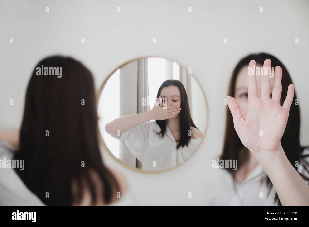 Junge Frau, die in den Spiegel schaut. Psychische Gesundheitsprobleme in Selbstisolation zu Hause. Depression, Angst, Phobie, Selbstmord und psychische Gesundheit Konzept. Stockfoto