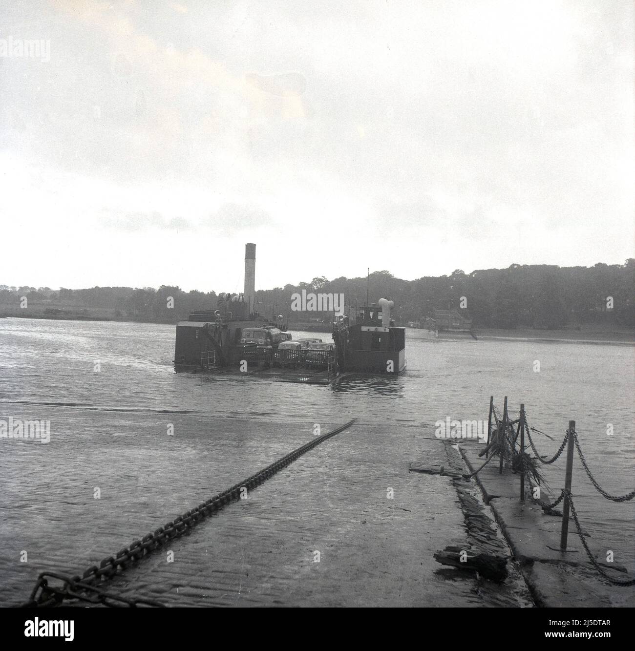 1961, historisch, Autos, ein Van und ein LKW der Epoche auf der Kettenfähre Erskine von 1936, dem Jahr, in dem sie vorgestellt wurde. Sie war eine dampfbetriebene, offene Fähre, die den Fluss Clyde überquerte, zwischen Erskine (Renfrawshire) und Old Kilpatrick (Clydebank), Schottland, Großbritannien. Die Kette, mit der das Schiff über das Wasser gelenkt wird, ist auf der Hellbahn zu sehen. Diese Fähre von Erskine lief bis 1962, nachdem sie eine frühere Fähre mit demselben Namen ersetzt hatte, und dann wurde bis 1971, als die Erskine-Brücke öffnete, ein neues Schiff (auch Erskine genannt) betrieben. Stockfoto