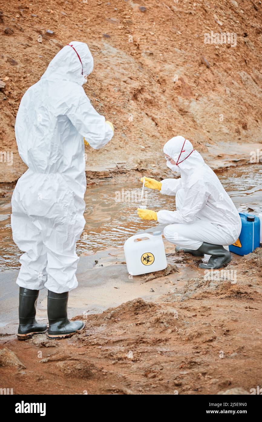 Ökologen, die bei der Probenahme von verschmutztem Wasser in gefährlichen Bereichen Schutzkleidung mit Pipetten tragen Stockfoto
