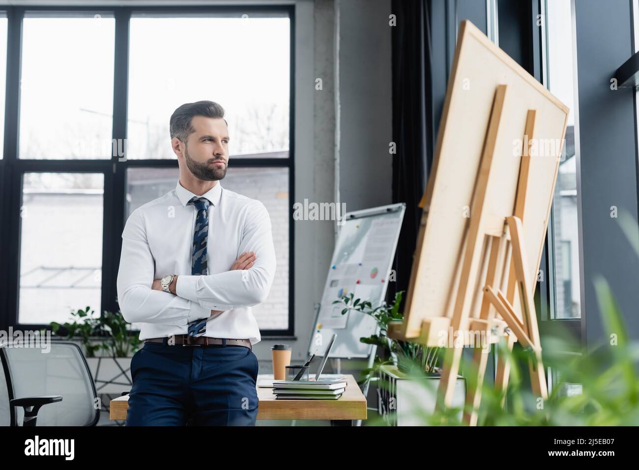 Ökonom im weißen Hemd, der mit gekreuzten Armen neben Flipcharts steht und wegschaut Stockfoto