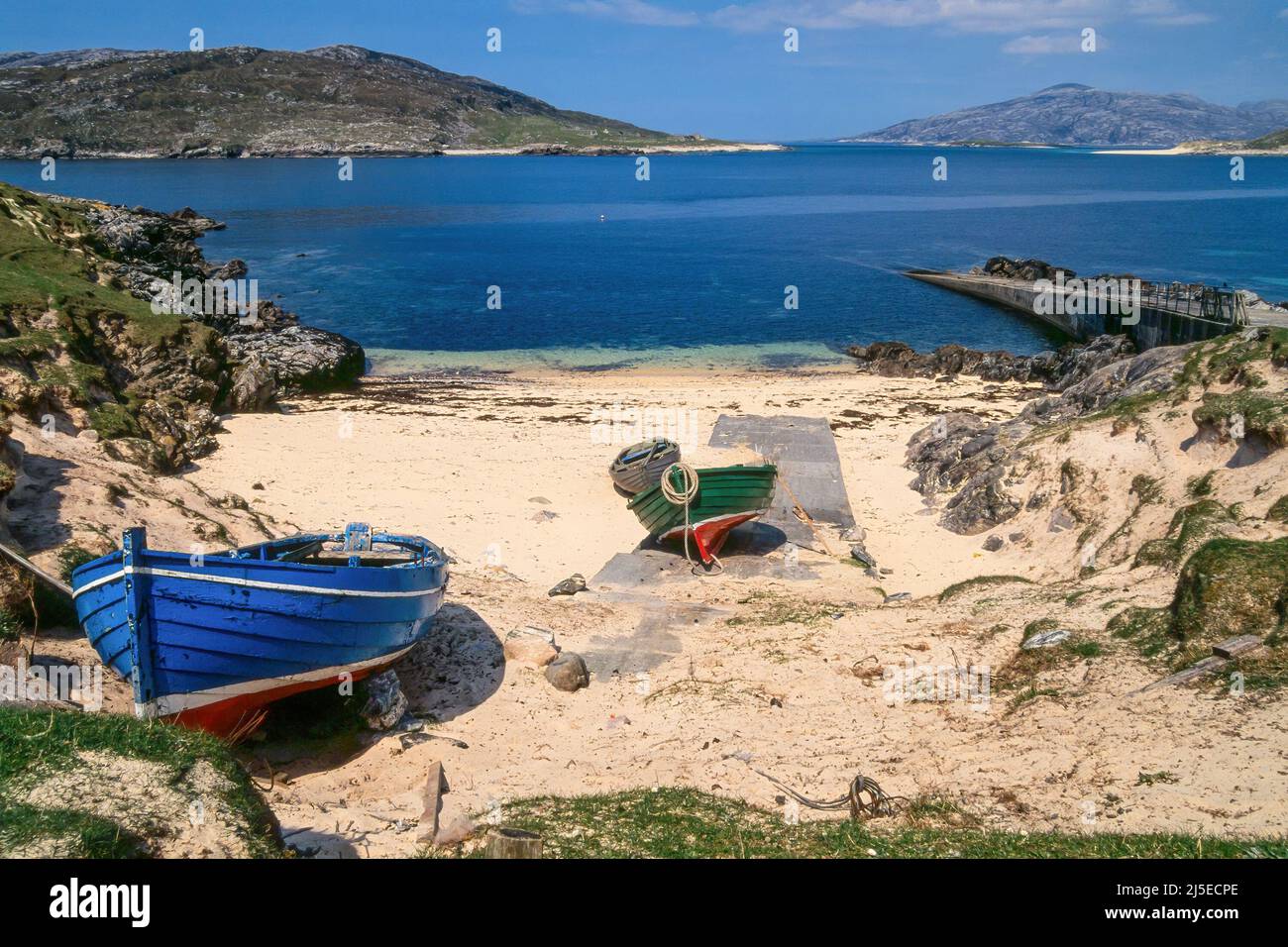 Kleine Boote über Helling und Anlegestelle in Port A' Tuath, Hushinish mit Caolas an Scarp und der Insel Scarp dahinter, Isle of Harris, Schottland, Großbritannien Stockfoto