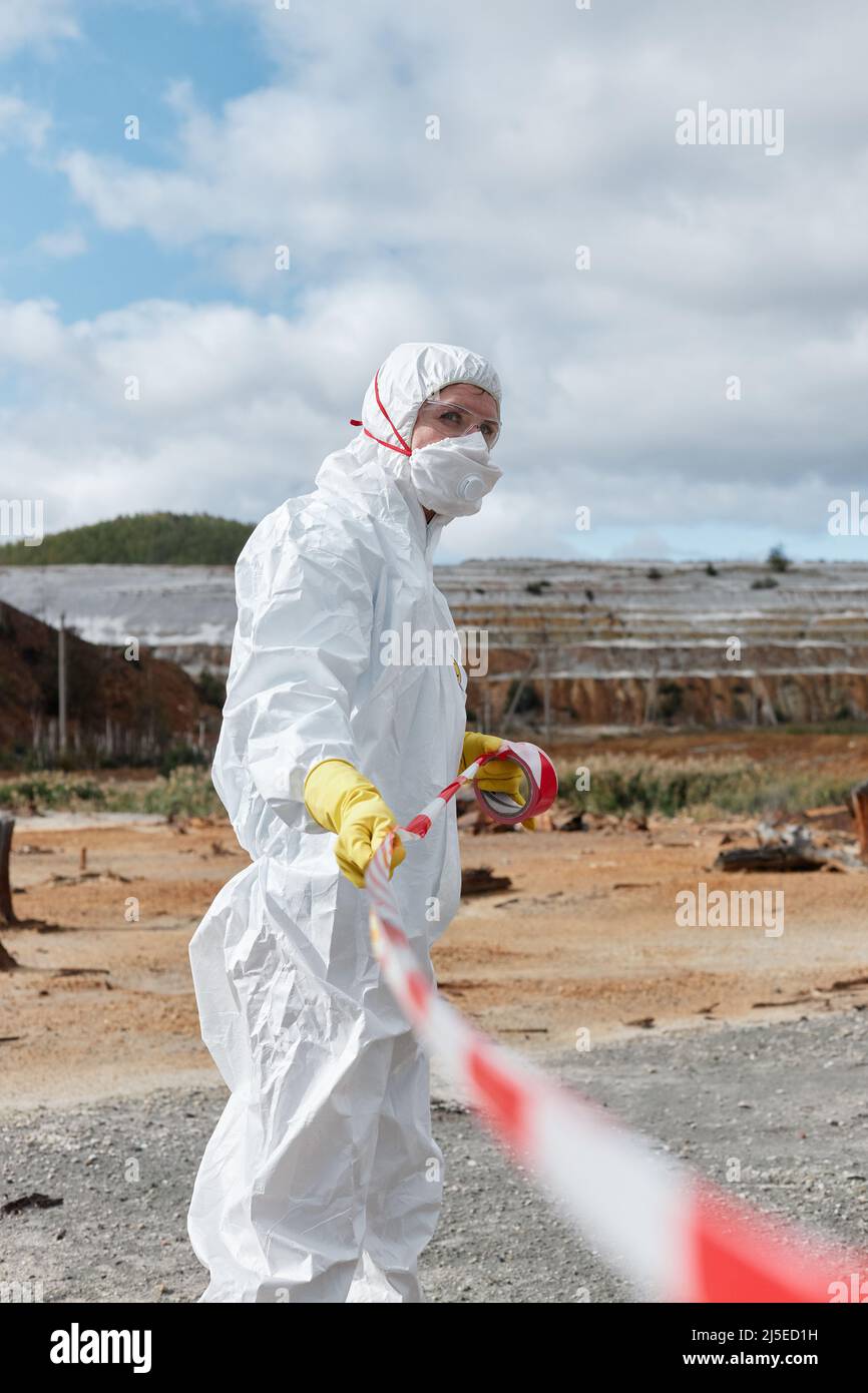 Spezialist für Umweltverschmutzung in Maske und Schutzanzug, der gefährliches Gebiet mit rotem und weißem Sperrband markiert Stockfoto