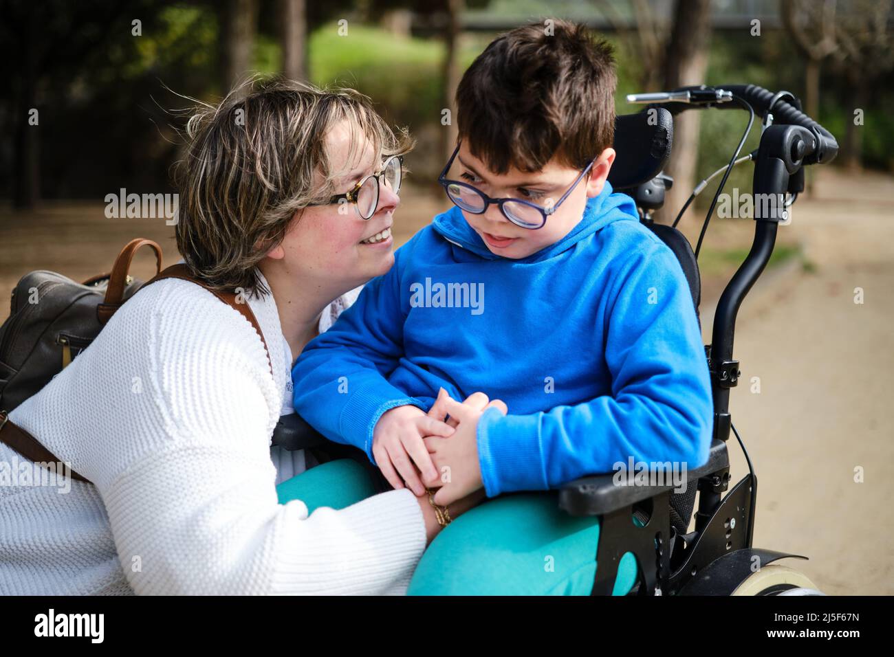 Behinderter Junge im Rollstuhl, der mit seiner Mutter einen Spaziergang im Freien genießt. Stockfoto