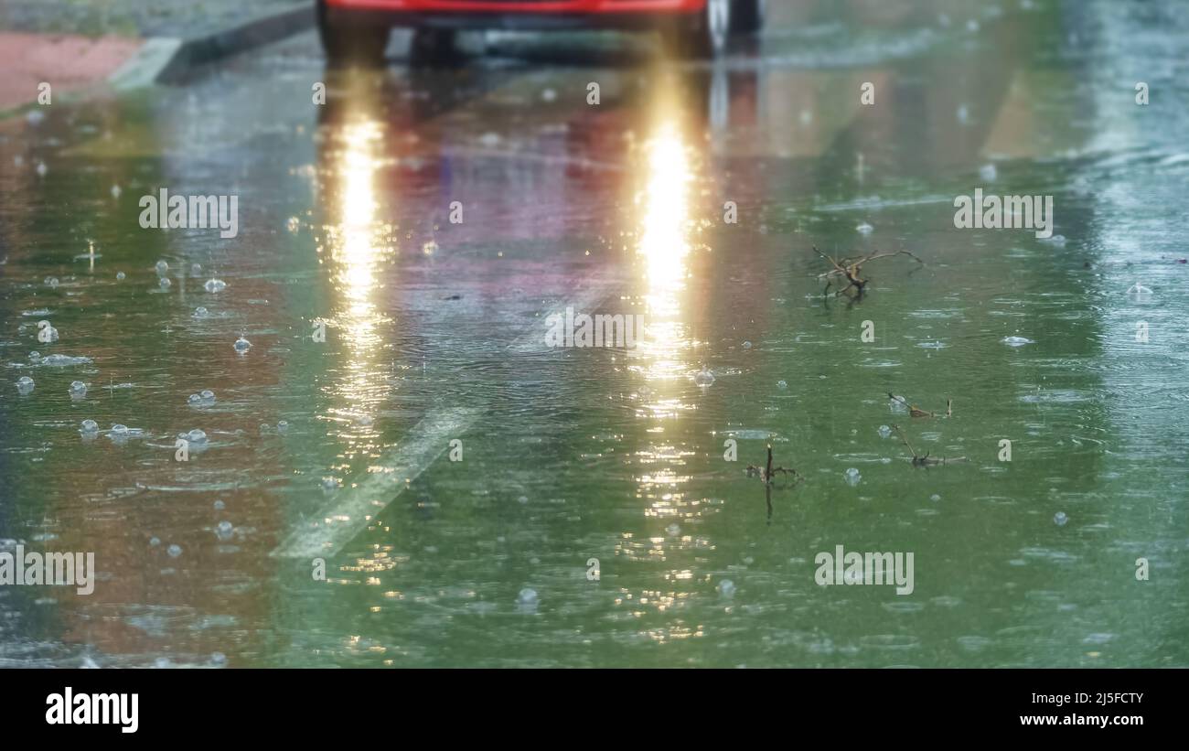 Regen fällt auf den Asphalt und Lichter im Auto erhellen die Szene. Stockfoto