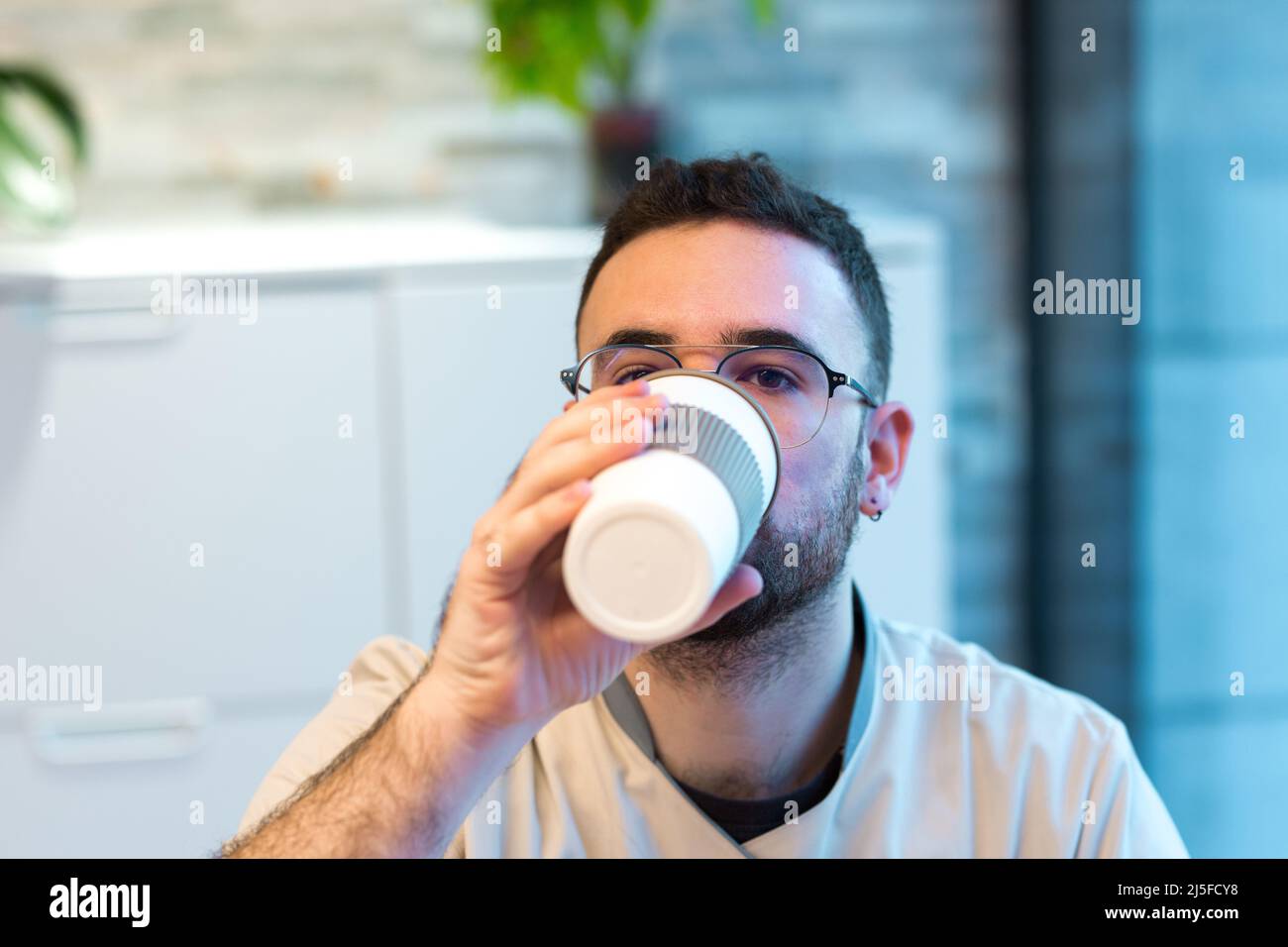 Der Rezeptionist trank in einer kurzen Pause Kaffee aus seiner wiederverwendbaren Tasse an der Rezeption Stockfoto