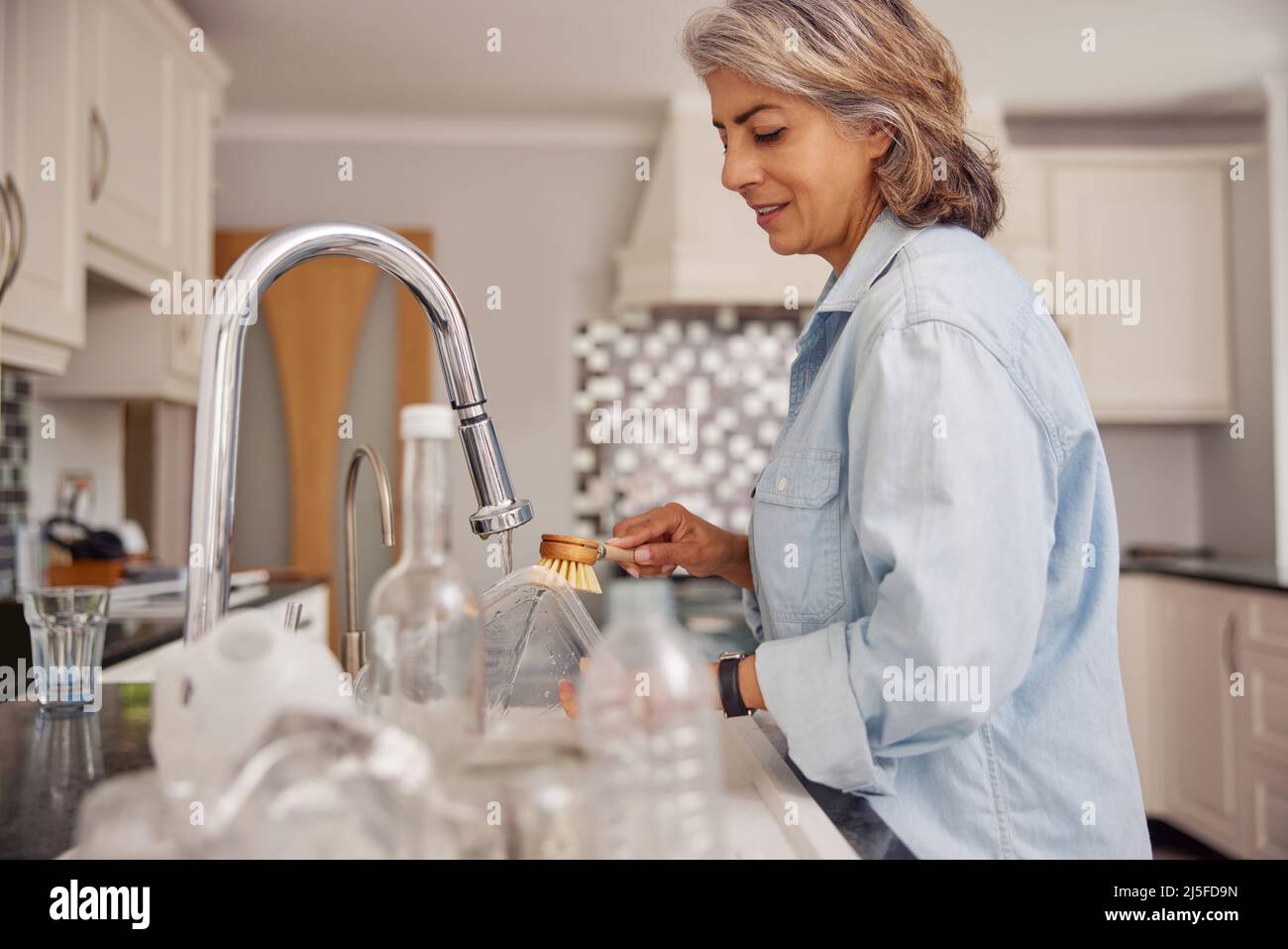 Reife Frau Zu Hause In Der Küche Waschen Gebrauchte Verpackung Vor Dem Recycling Stockfoto