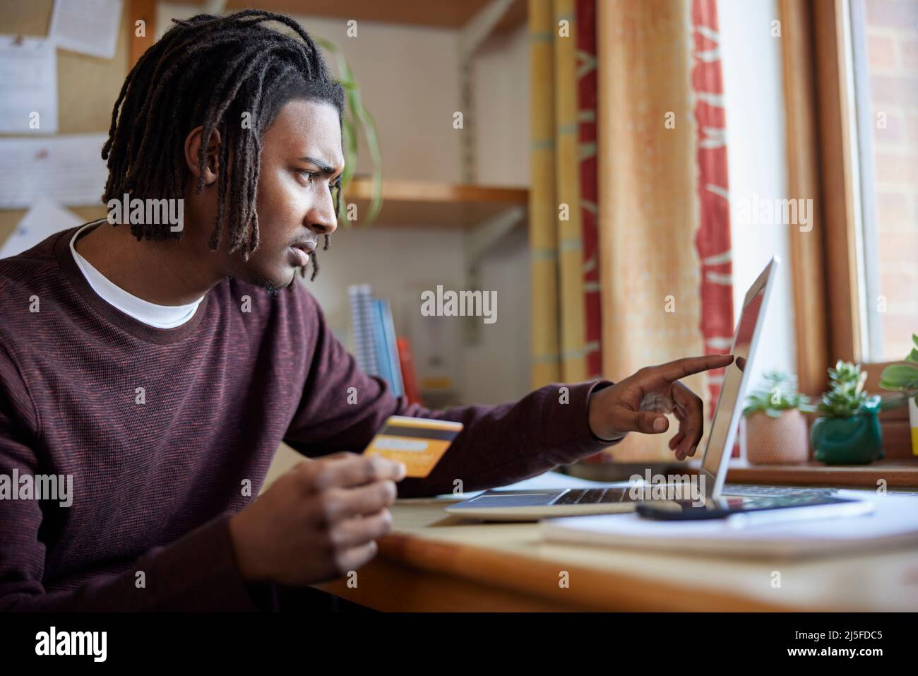 Männliche Universität Oder College-Student Mit Kreditkarte Blick Auf Laptop Besorgt Über Schulden Am Schreibtisch Im Zimmer Stockfoto