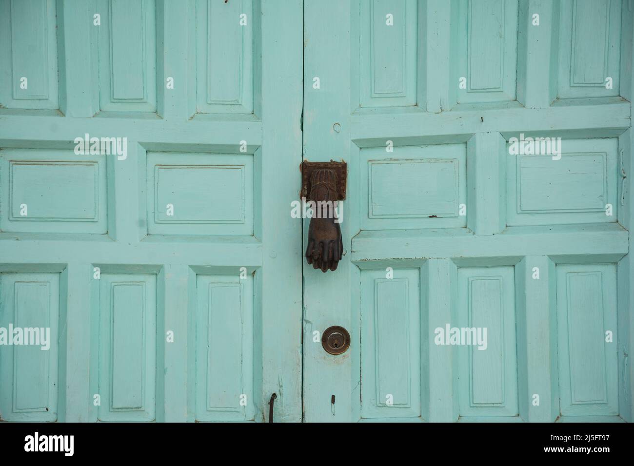 Goldener, handgeformter Klopfer an einer türkisfarbenen, rustikalen Tür. Isoliertes Detail Stockfoto