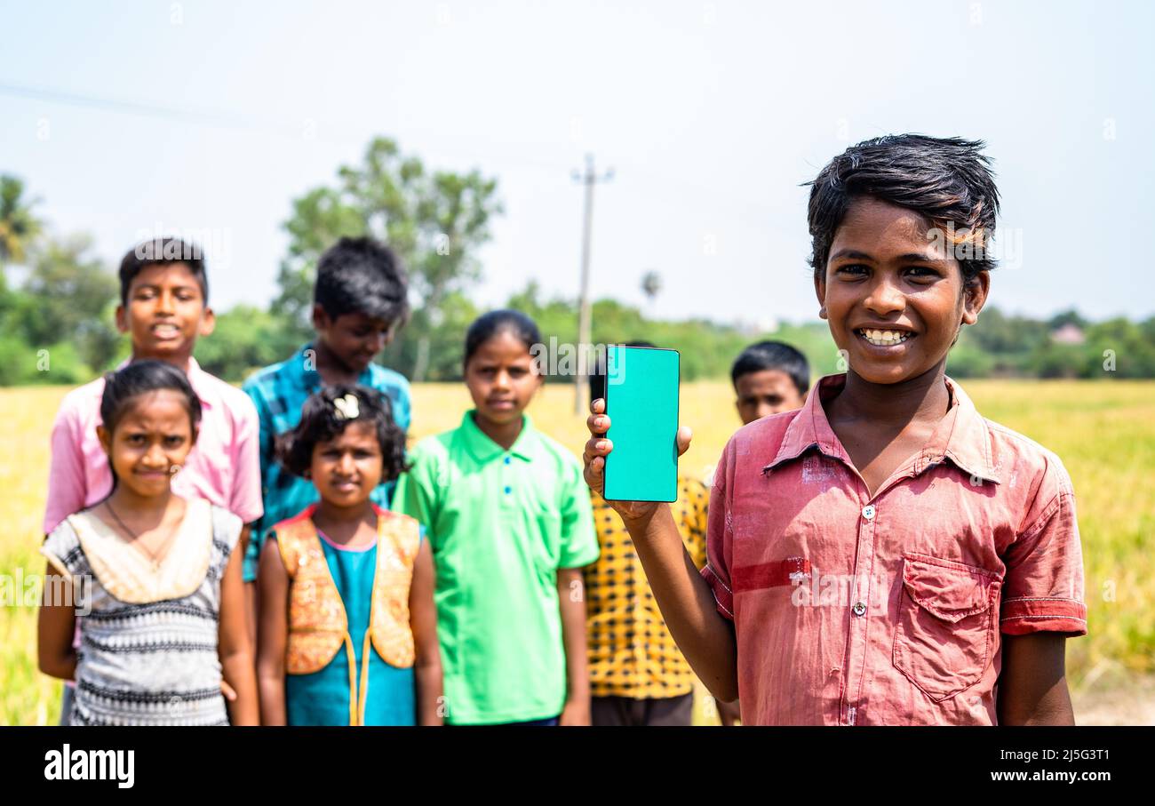 Glückliches lächelndes Dorfkind, das grünes Handy vor den Kindern zeigt, indem es Kamera sucht - Konzept der Bildung, App-Werbung für lerning Stockfoto